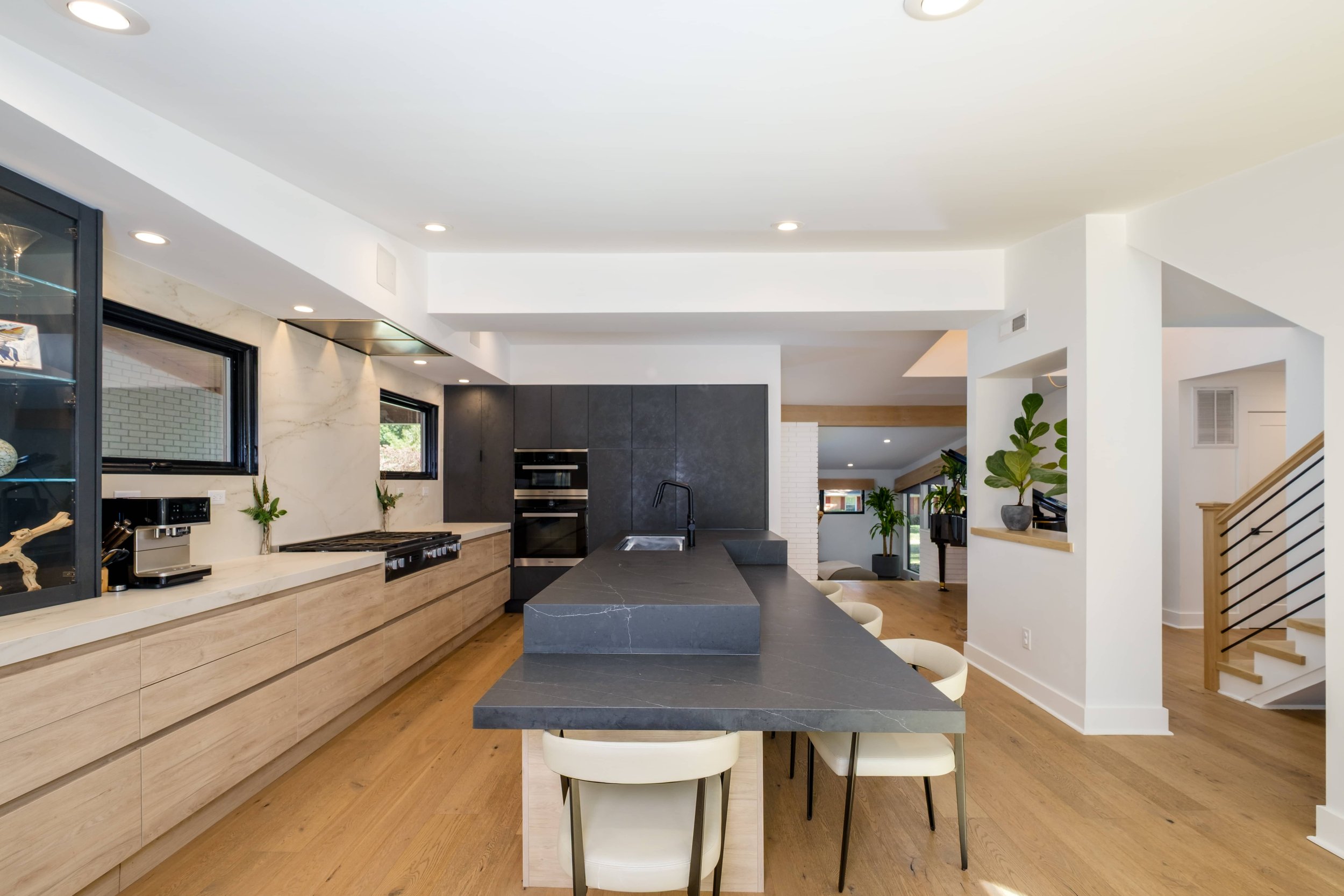 Modern kitchen with light wood lower cabinets, black upper cabinets, a long dark gray stone island with seating, and light wood flooring