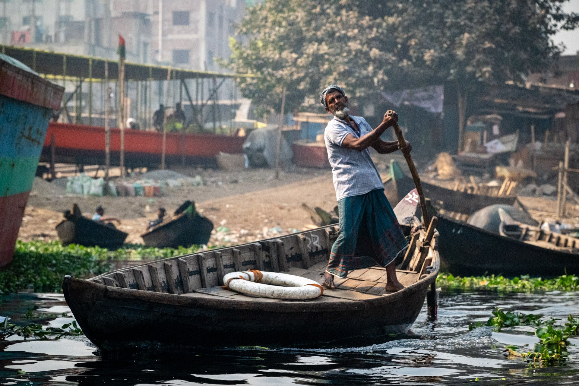 The captain of the sampan as he brings commuters cross the Buriganga River in Dhaka, Bangladesh.  These are small, traditional wooden boats powered and steered by a single oar.