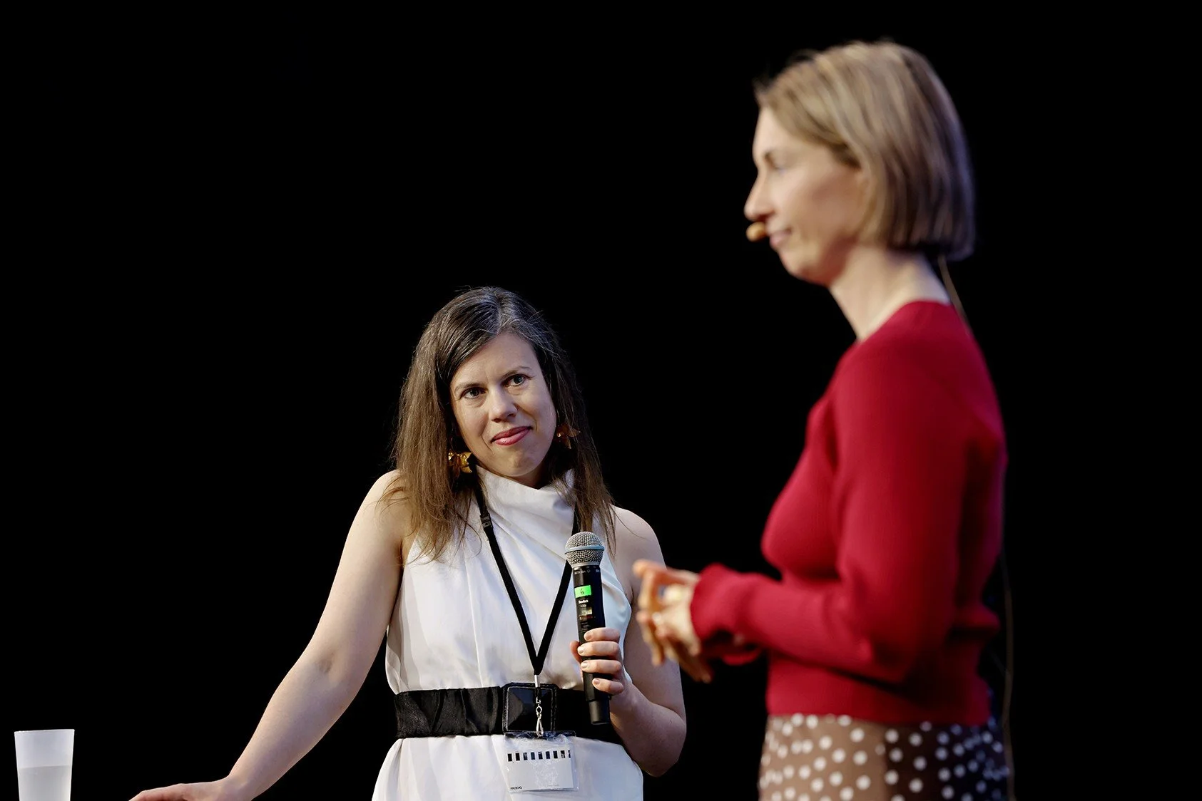 Lisa Martin in conversation on a stage holding a microphone while interviewing a keynote speaker.