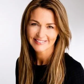 Smiling woman with long brown hair wearing a black top, against a light background.