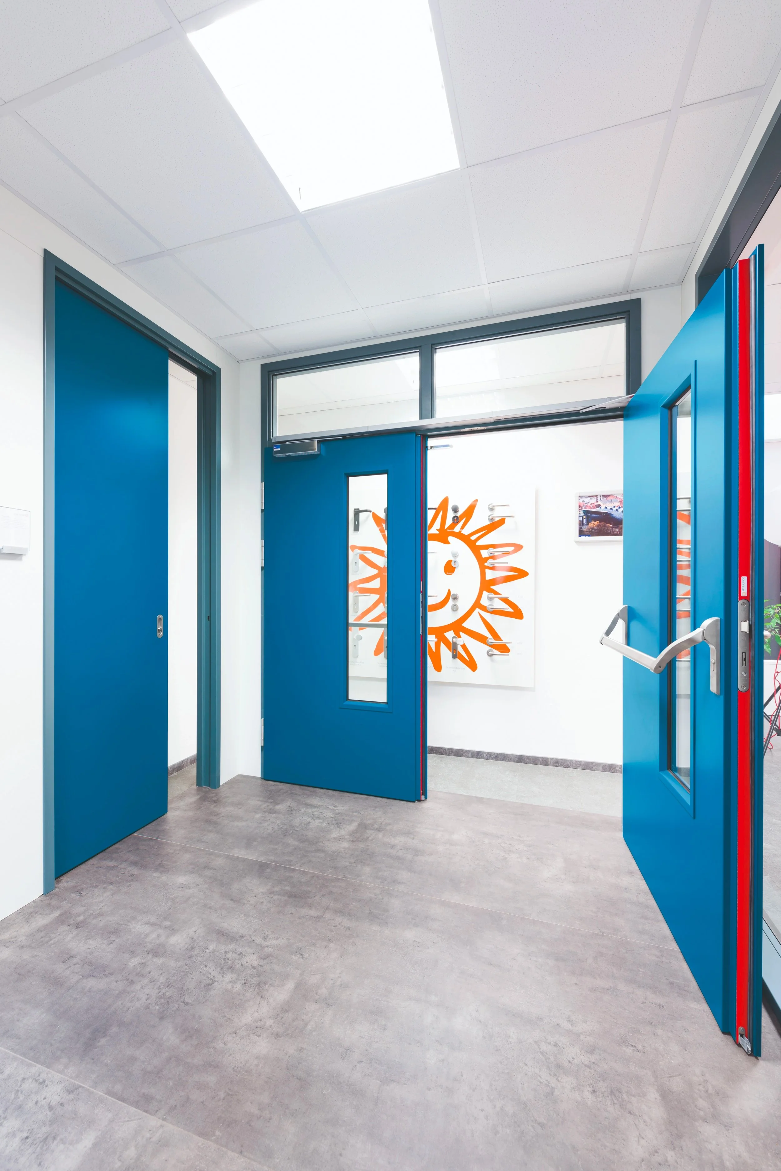 Innenansicht eines modernen Gebäudes mit blauen Türen und einem Kunstwerk an der Wand, das eine lächelnde Sonne zeigt.