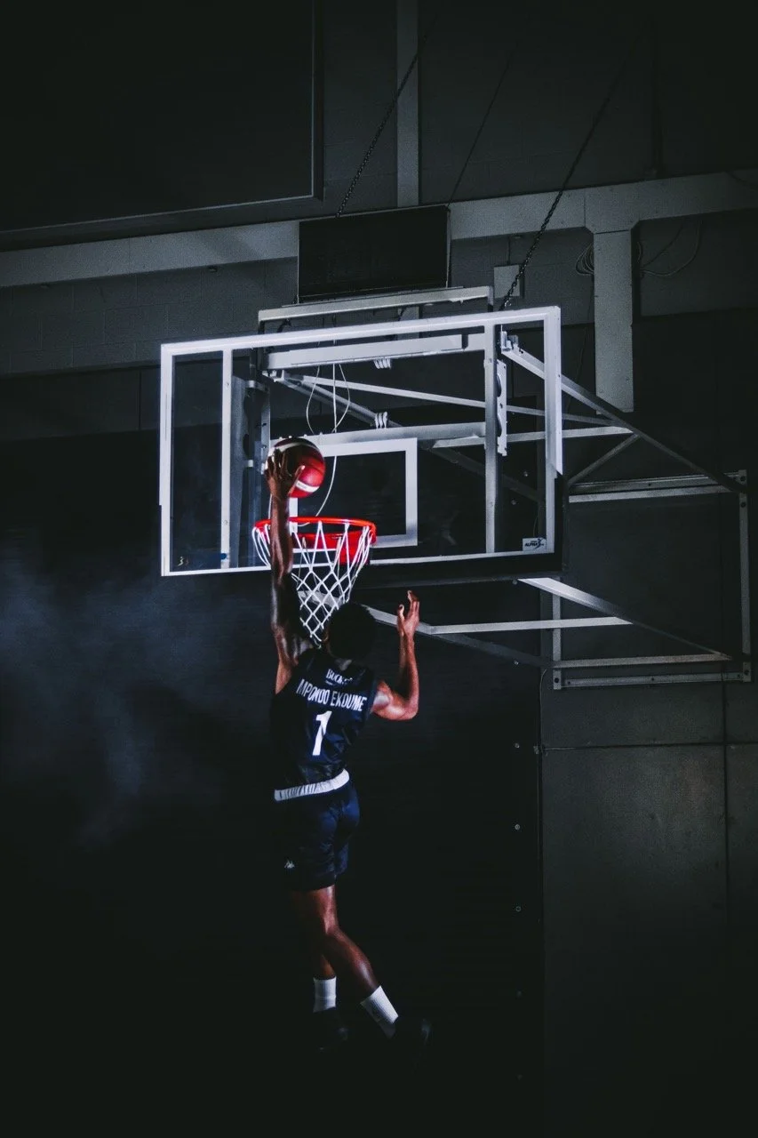 A basketball player is jumping towards the hoop to make a shot in a dimly lit gym.