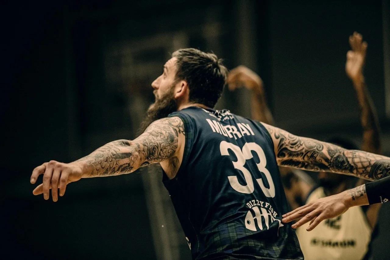 A man with a tattooed arm wearing a sports jersey with the name Murray and number 33, extending his arms in a dance or celebration.