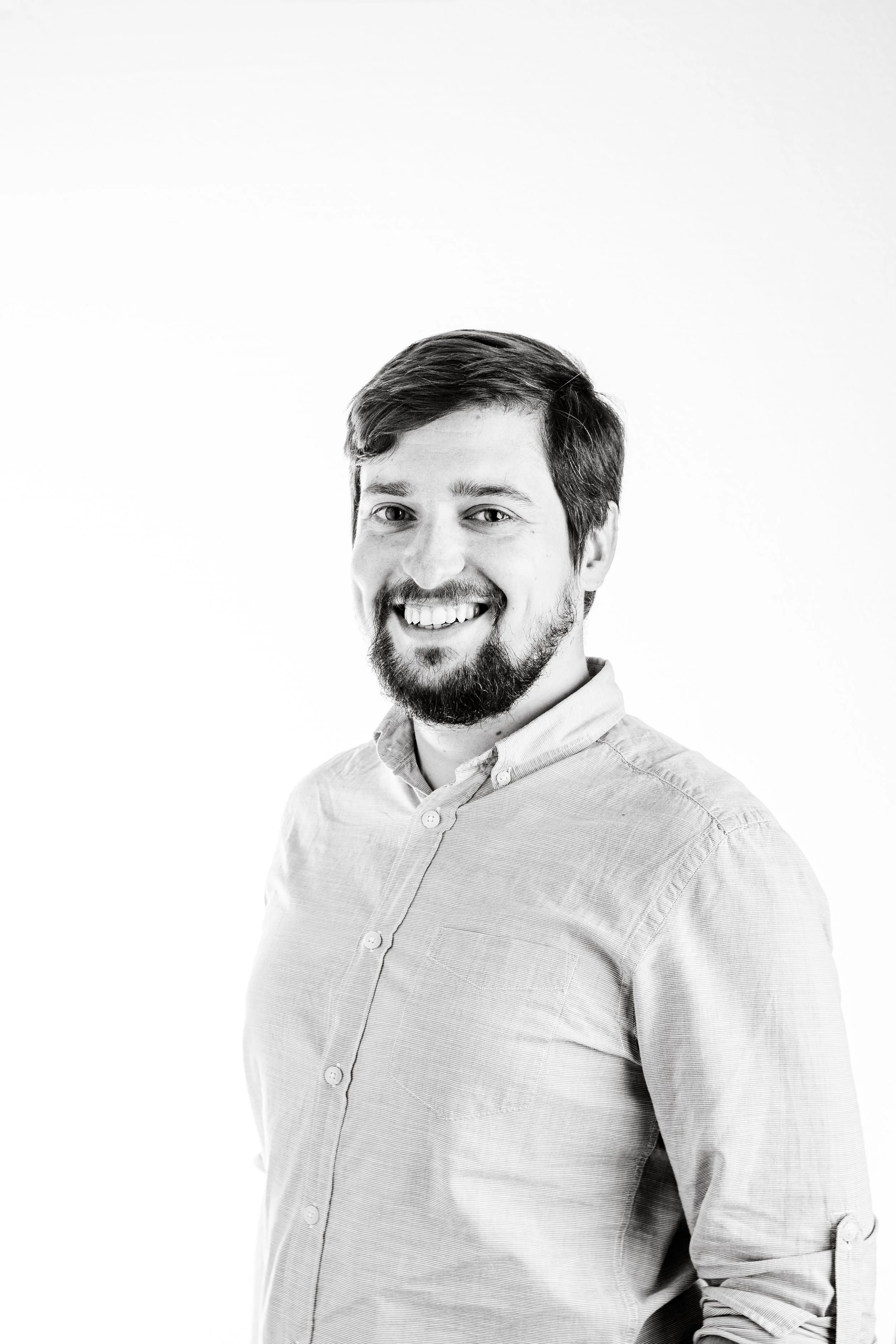 Black and white portrait of a smiling man with short hair and a beard, wearing a buttoned-up shirt, against a plain white background.