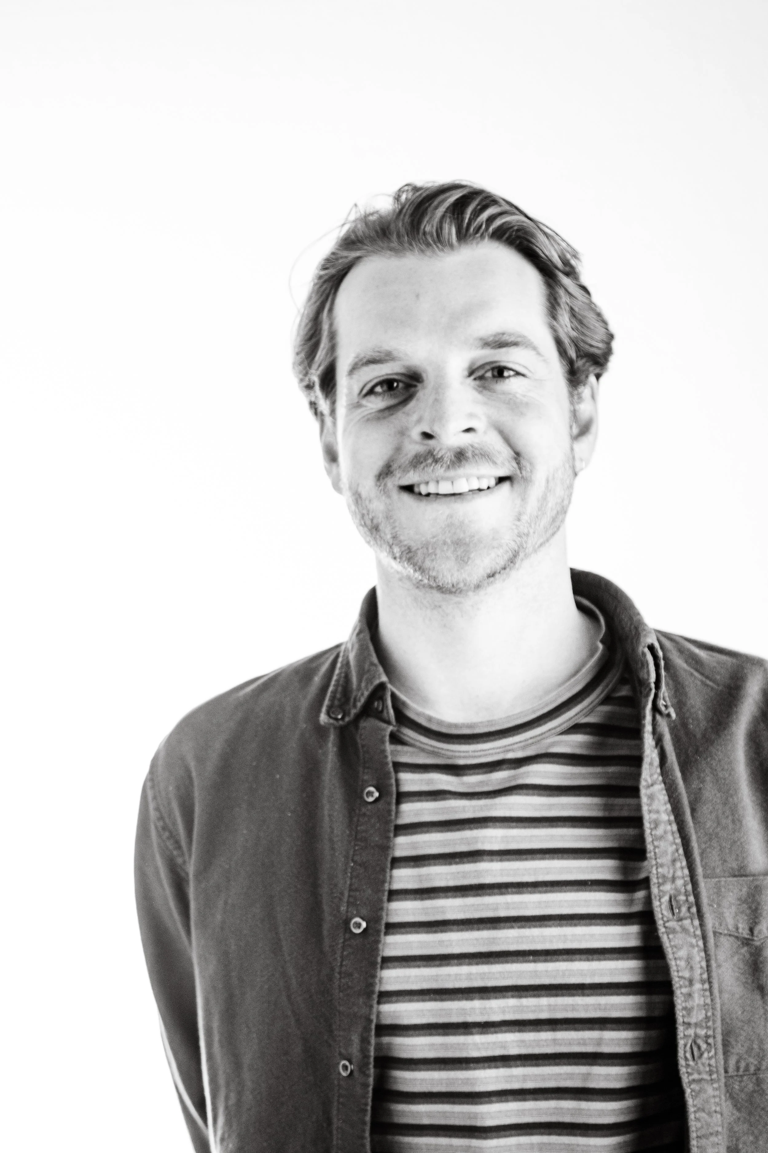 Black and white portrait of a man smiling, wearing a striped shirt and a casual jacket.