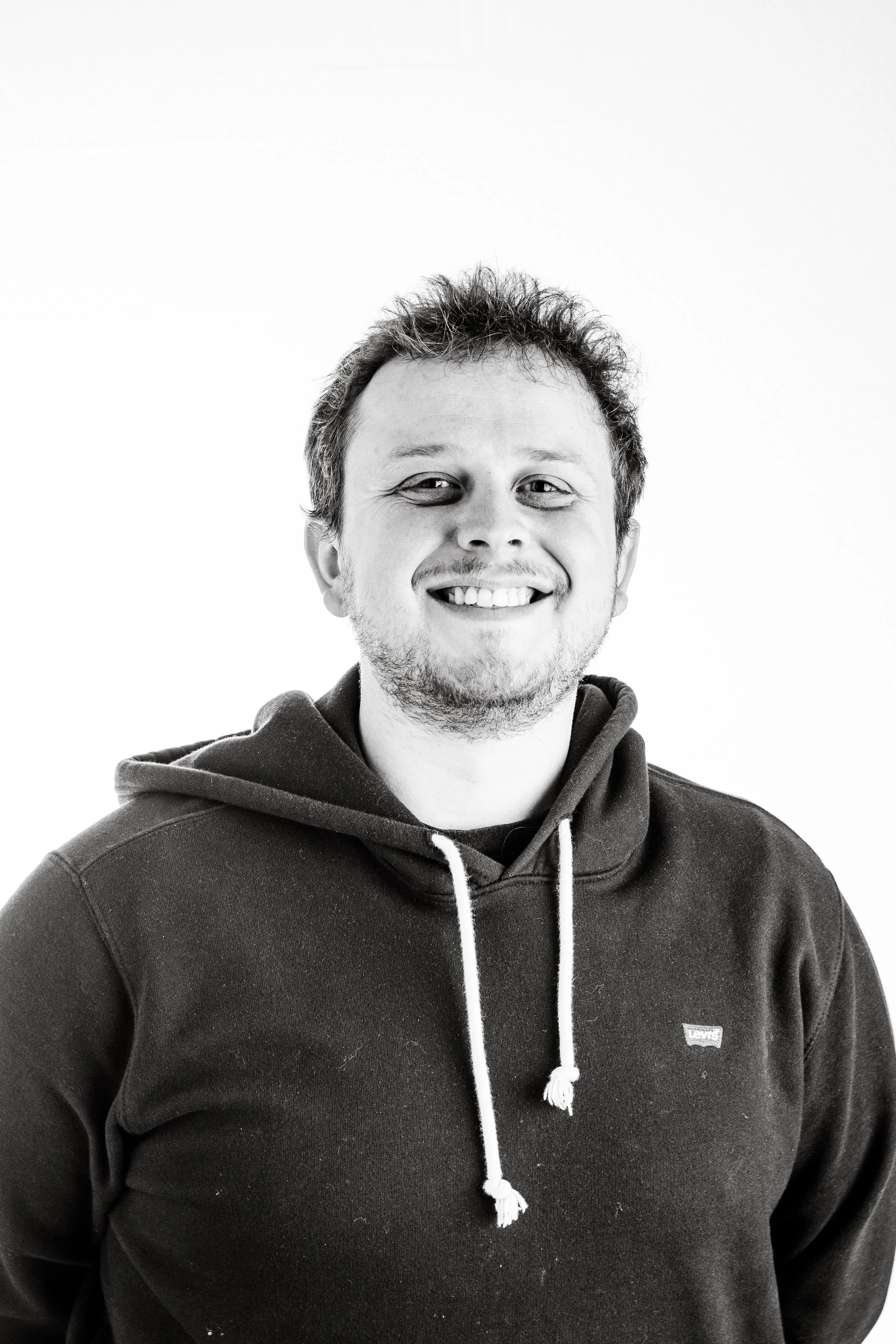 Black and white portrait of a smiling man wearing a hoodie.