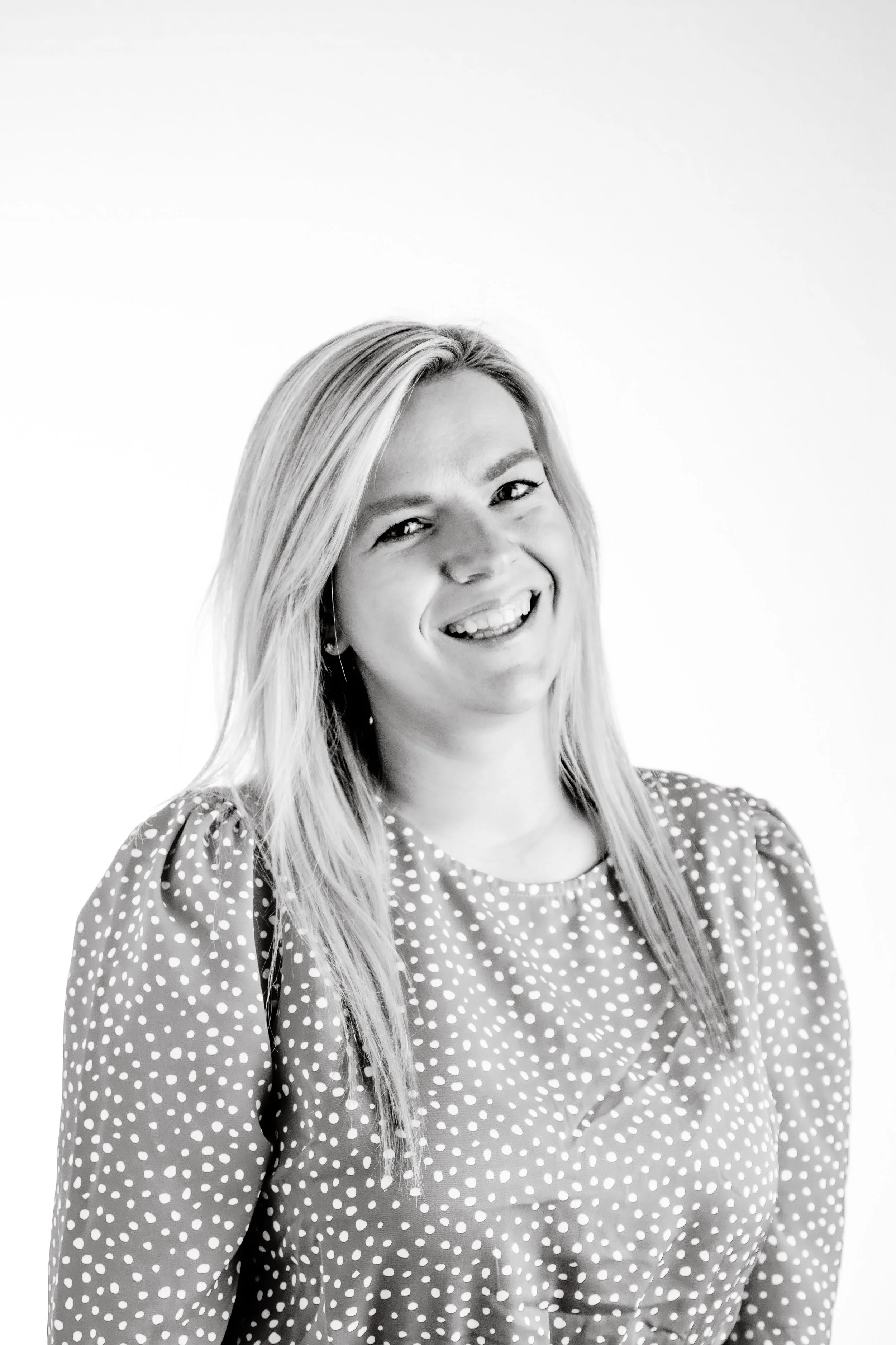 Black and white photo of a smiling woman with shoulder-length hair wearing a polka dot blouse.
