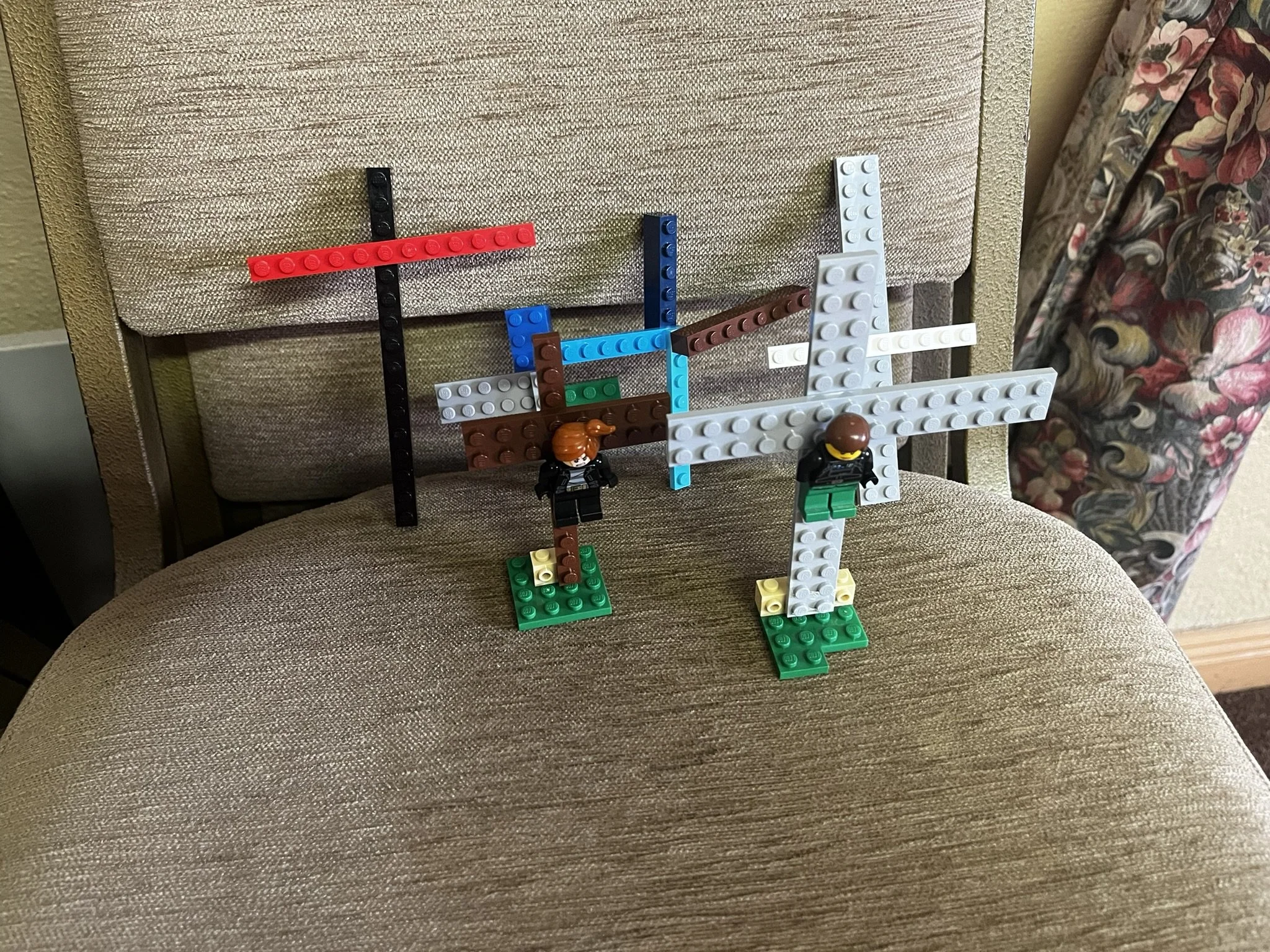 Lego structures built on a chair, with two Lego figures standing on green bases, and various bricks arranged to resemble a complex structure.