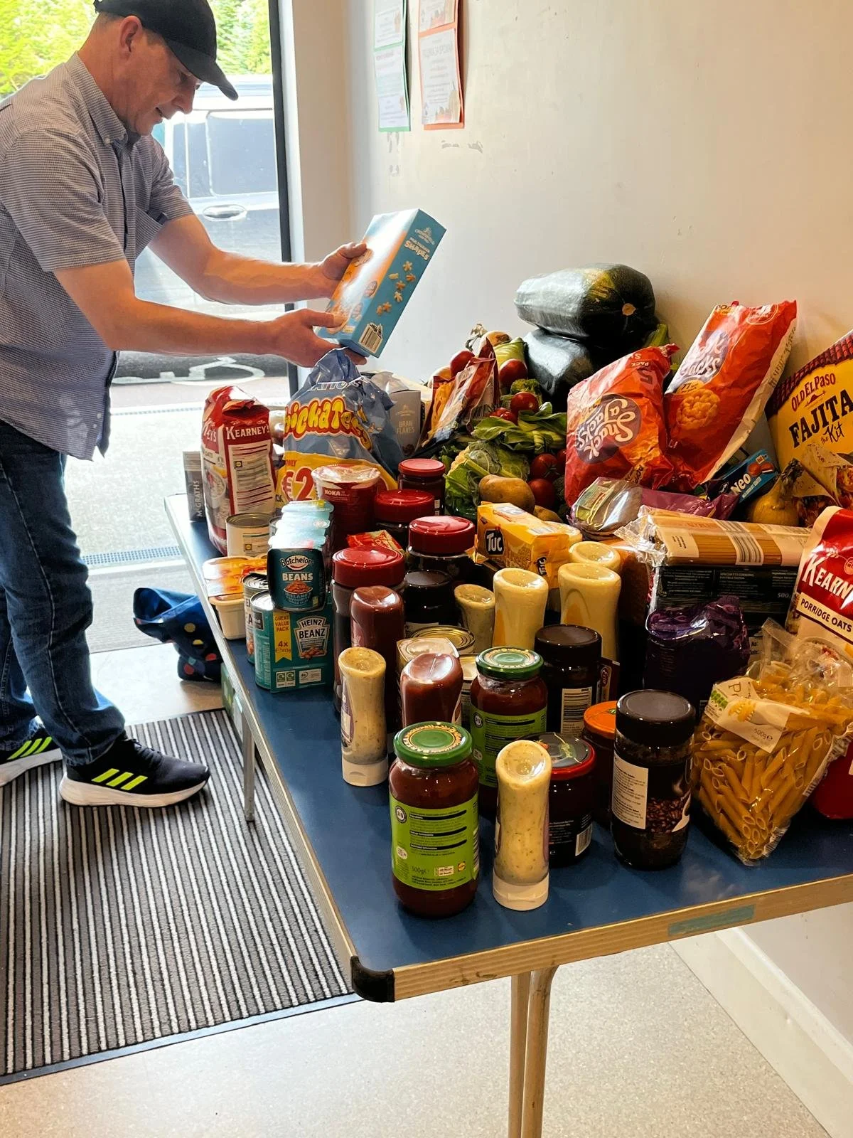 Man organizing canned and bottled food items on a table outside a grocery store.