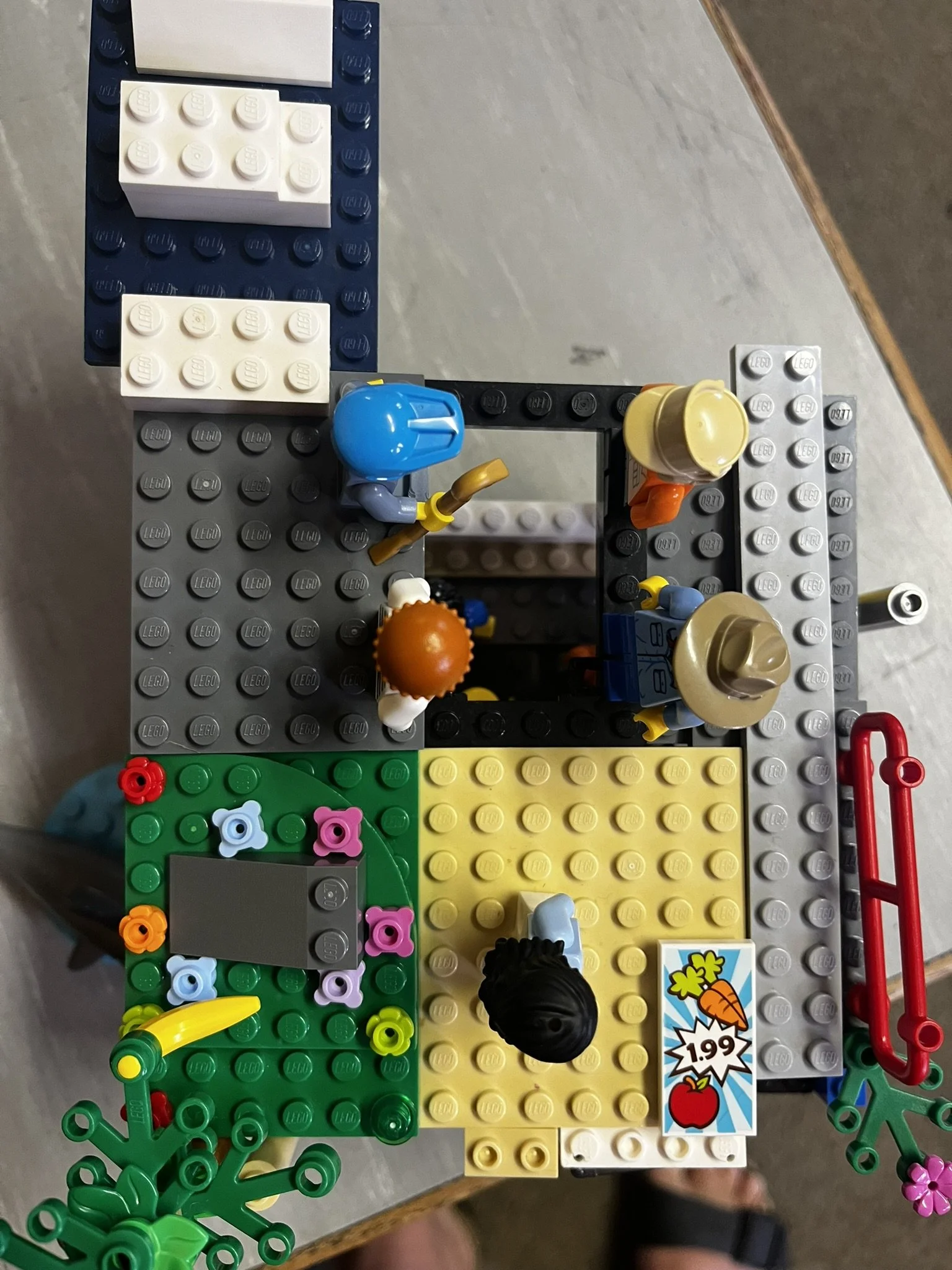 Lego scene with mini figures, colorful blocks, and a sign showing a carrot and apple with a price of $1.99