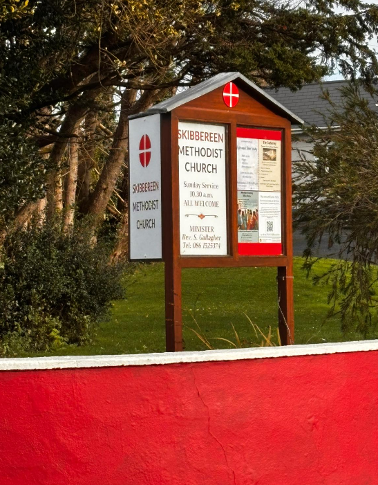 Church sign for Skibbereen Methodist Church with information about Sunday service at 10:30 a.m., featuring the Methodist cross symbol, surrounded by trees and greenery.