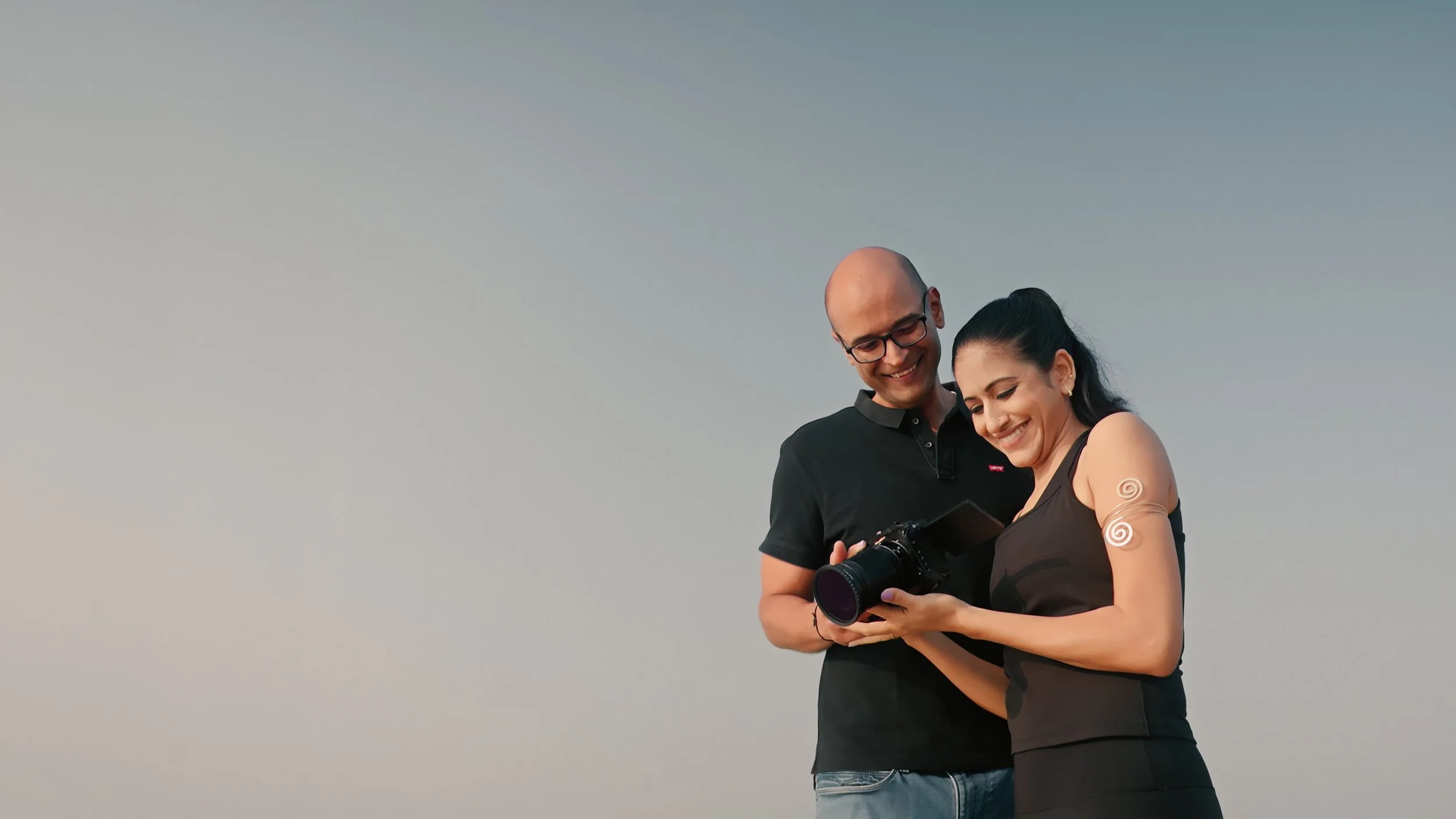 A couple in traditional Indian attire pouring sand, smiling at each other against a dark background.