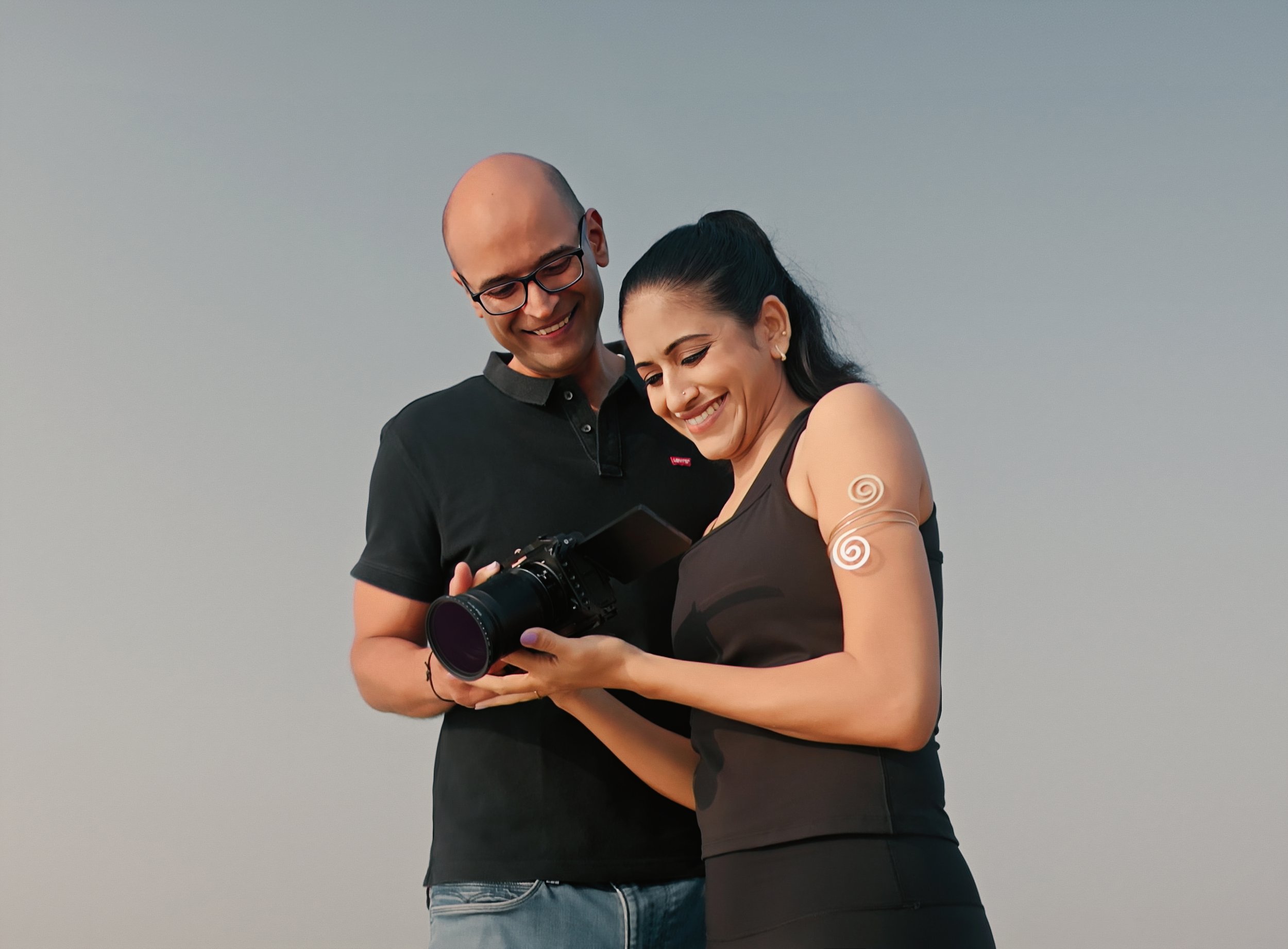 A couple in traditional Indian attire pouring sand, smiling at each other against a dark background.