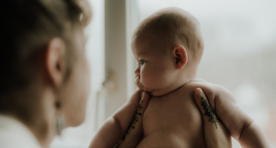 A person holding a baby near a window, with the baby looking intently at the person.