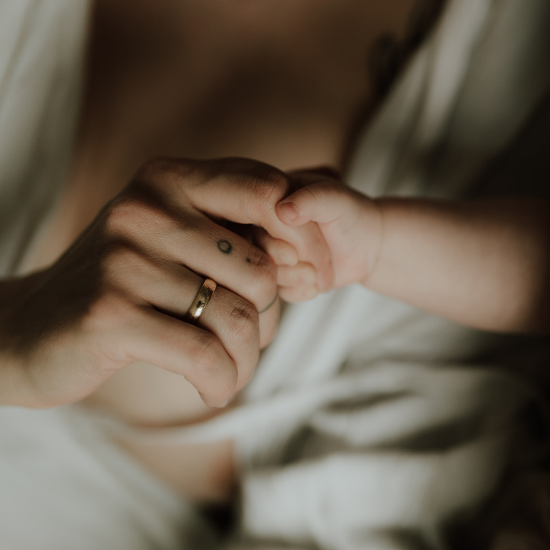 Close-up of an adult hand holding a baby's hand, both hands showing rings and tattoos.
