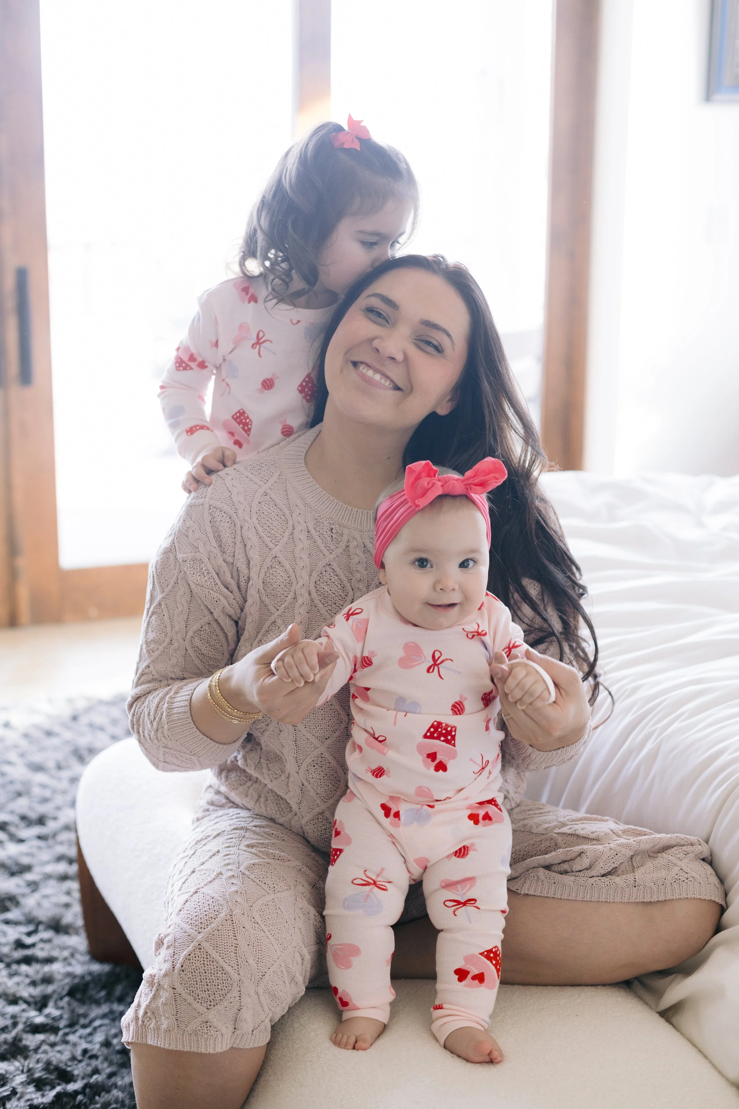 Woman laughing, wearing a patterned cardigan, white top, black leggings, hat, and sneakers, standing against a plain background.