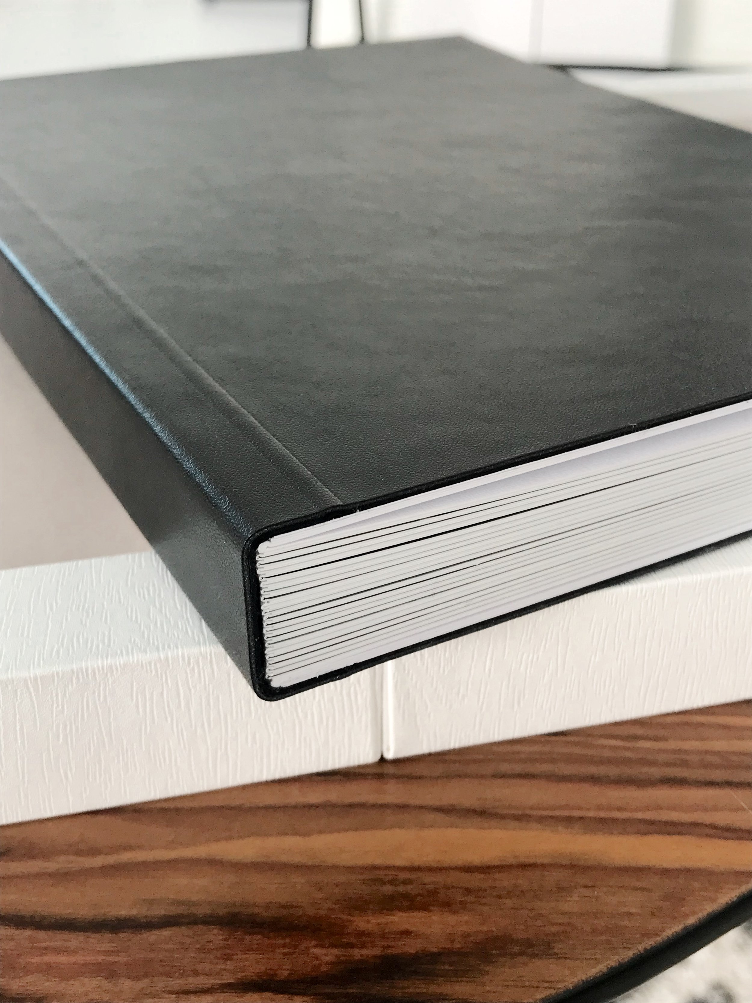 Black hardcover book on wooden table, white box beneath