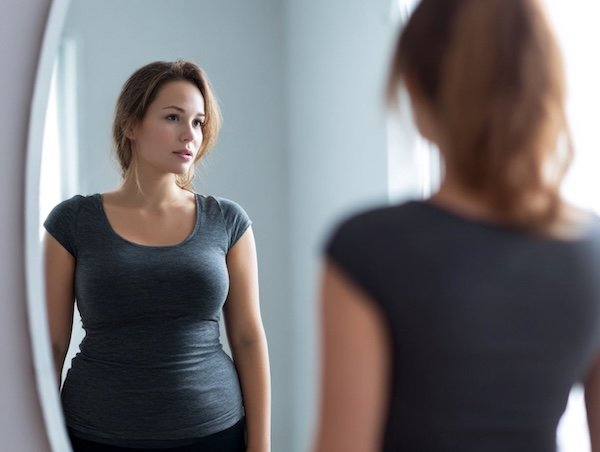 A woman looking at herself in the mrror suffering from body dysmorphia while using ozempic, wegovy or GPL1s.