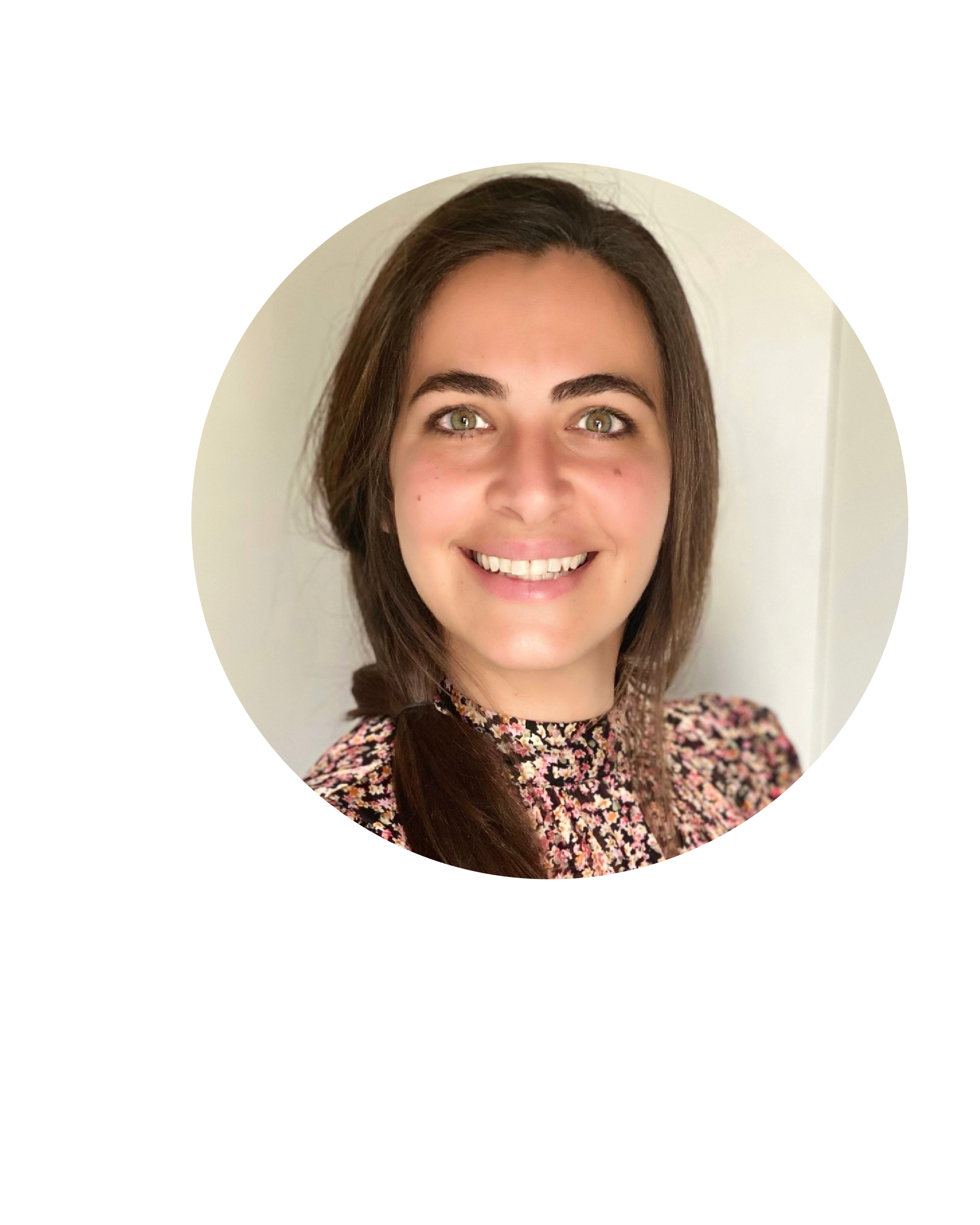 Smiling woman with medium brown hair, green eyes, and light skin, wearing a floral patterned top, standing against a neutral background.