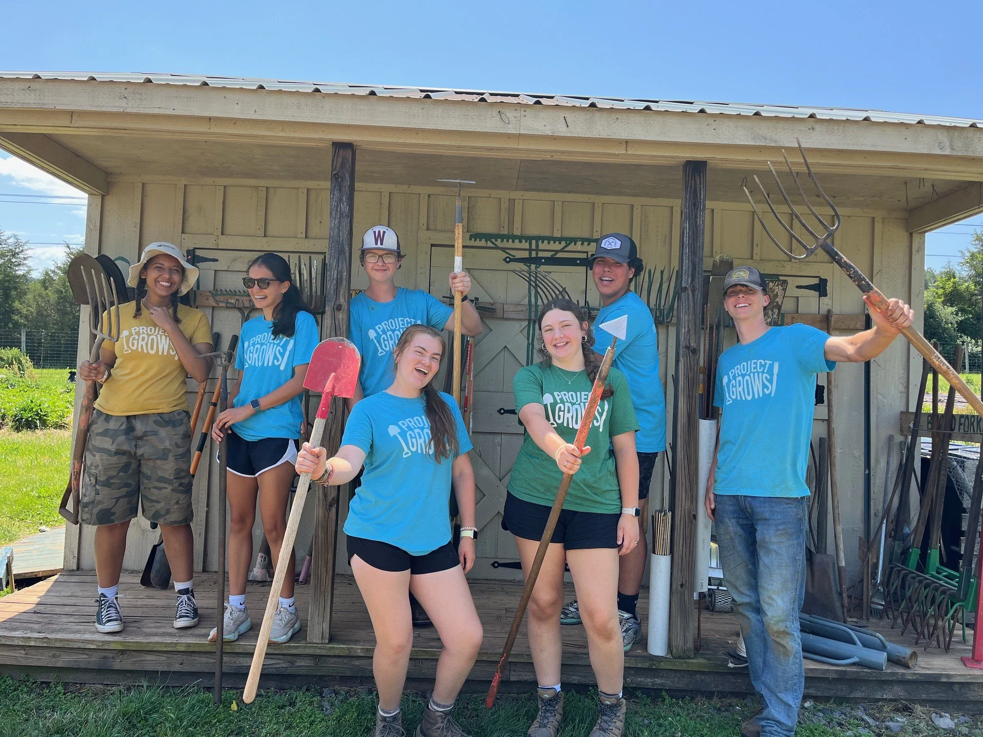 Youth holding up gardening tools in front of shed