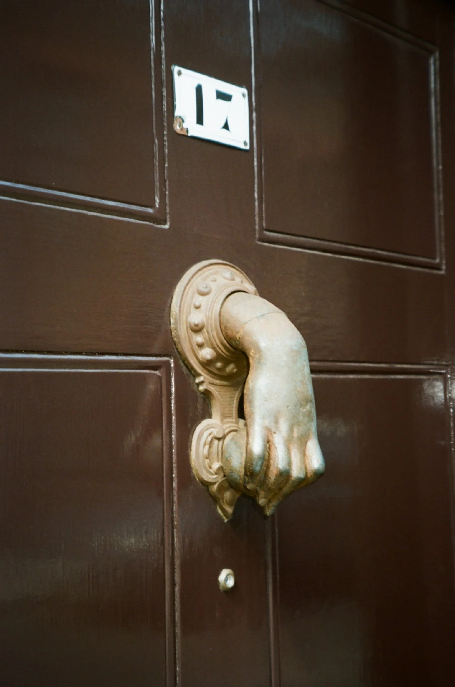 Close-up of a brown wooden door with the number 17 and a decorative brass door knocker shaped like a hand.