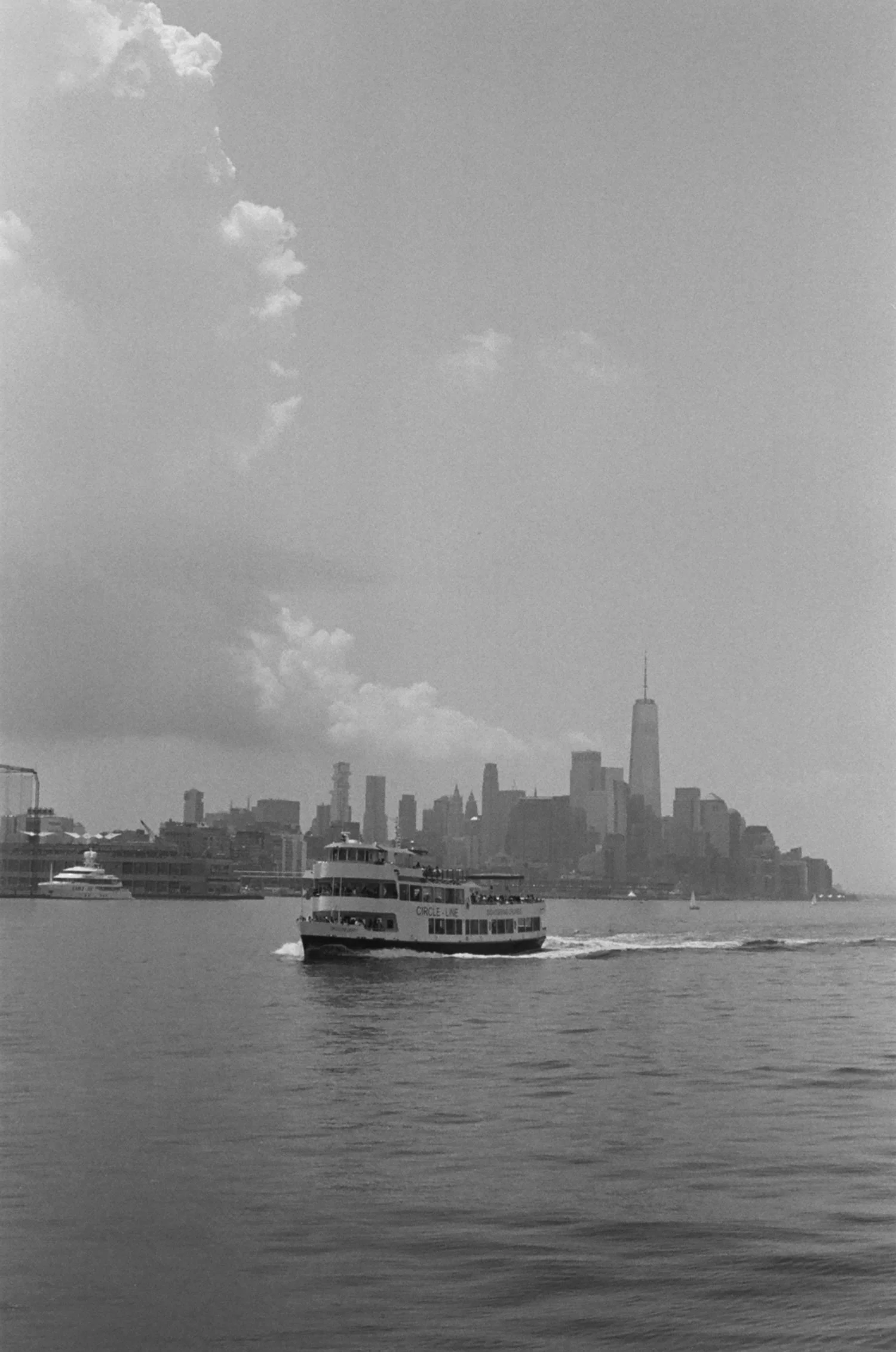 A boat sailing on the river with New York City skyline, including One World Trade Center, in the background.