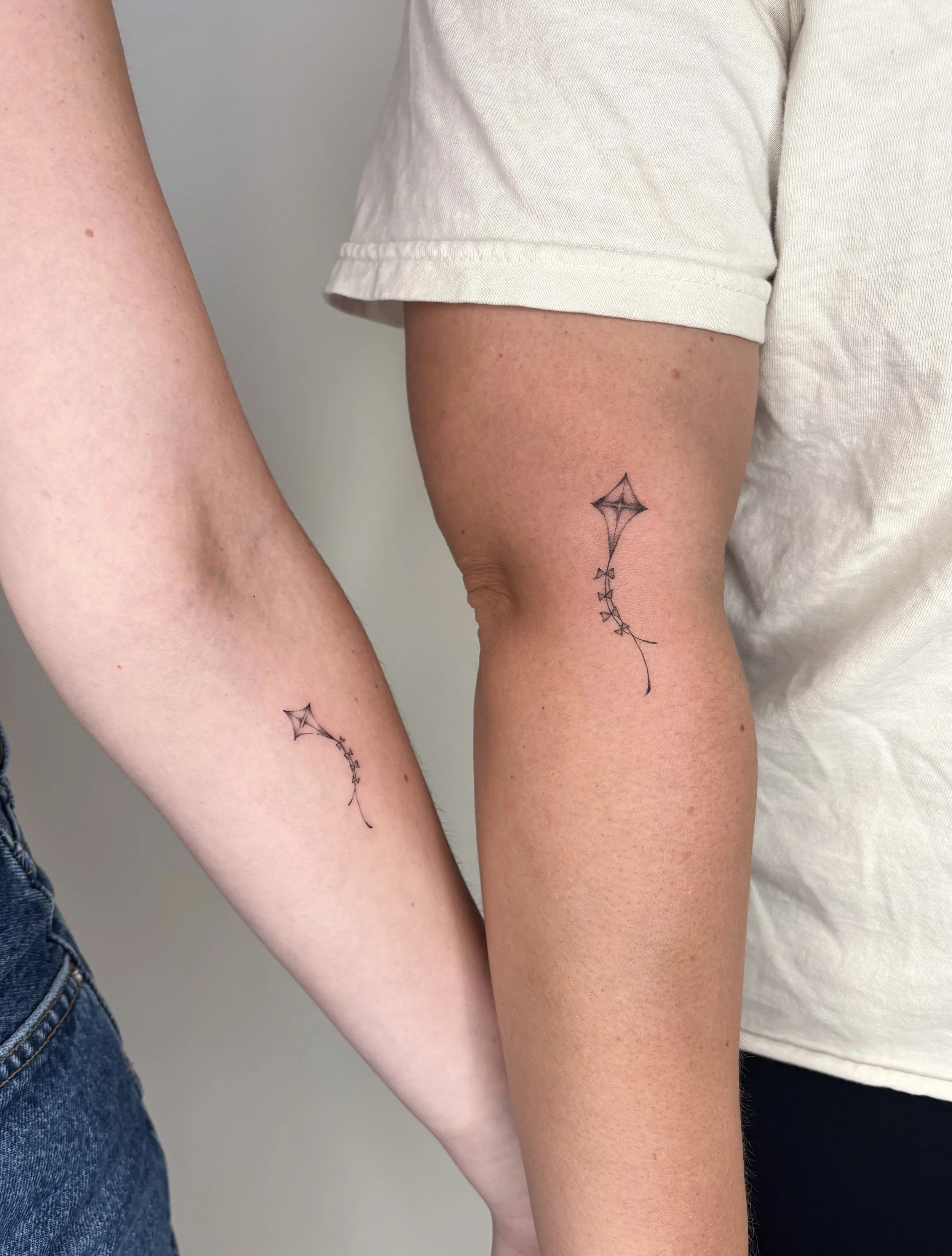 Two people with tattoos of matching kites.