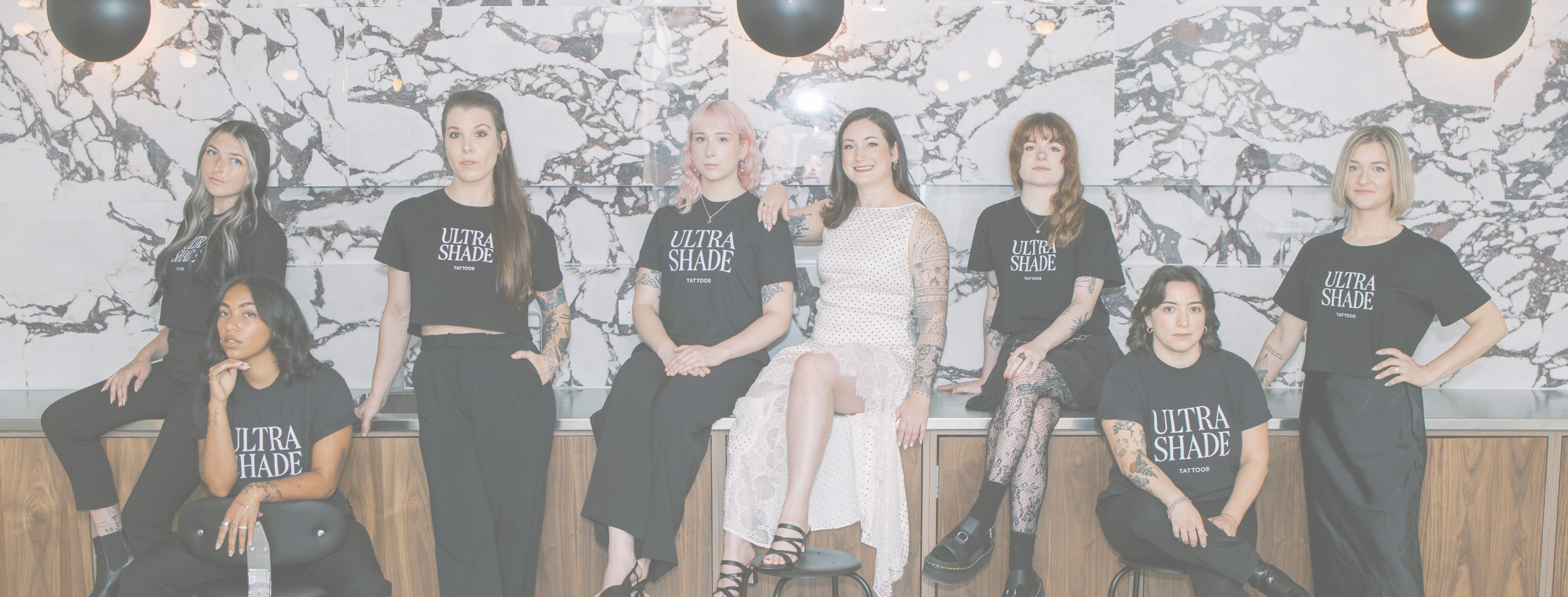 The Ultrashade Tattoos team of 8 people posing together inside their modern tattoo studio, showcasing the artists in a professional group portrait.