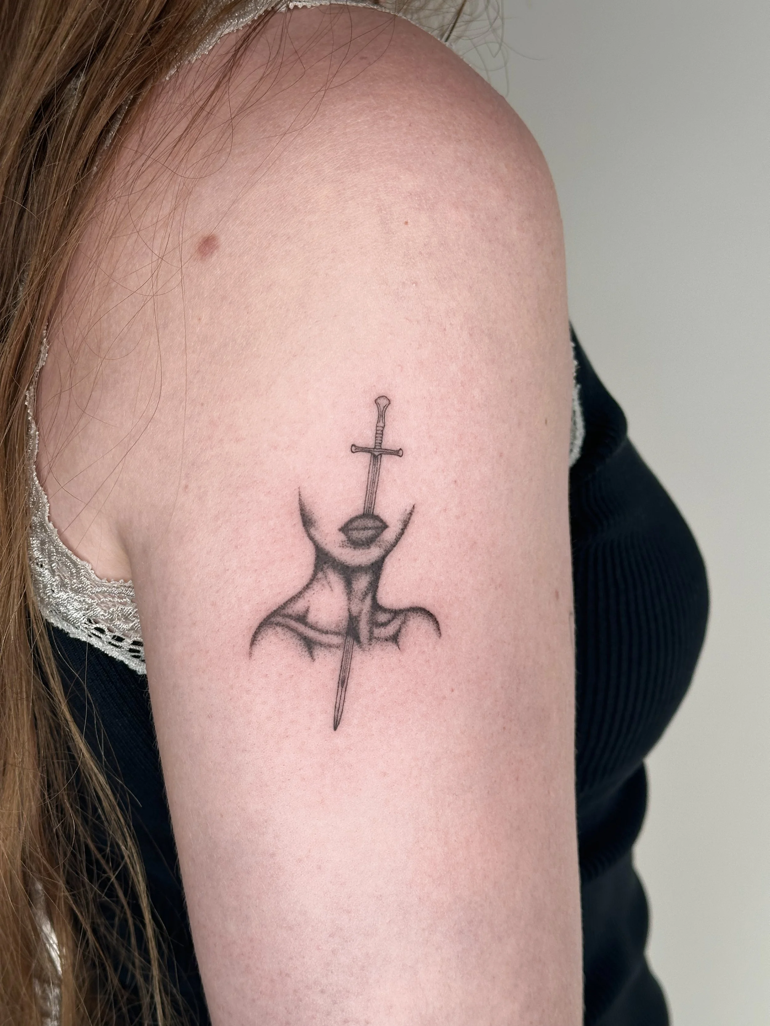 Tattoo of a sword piercing a mask on a person's upper arm.
