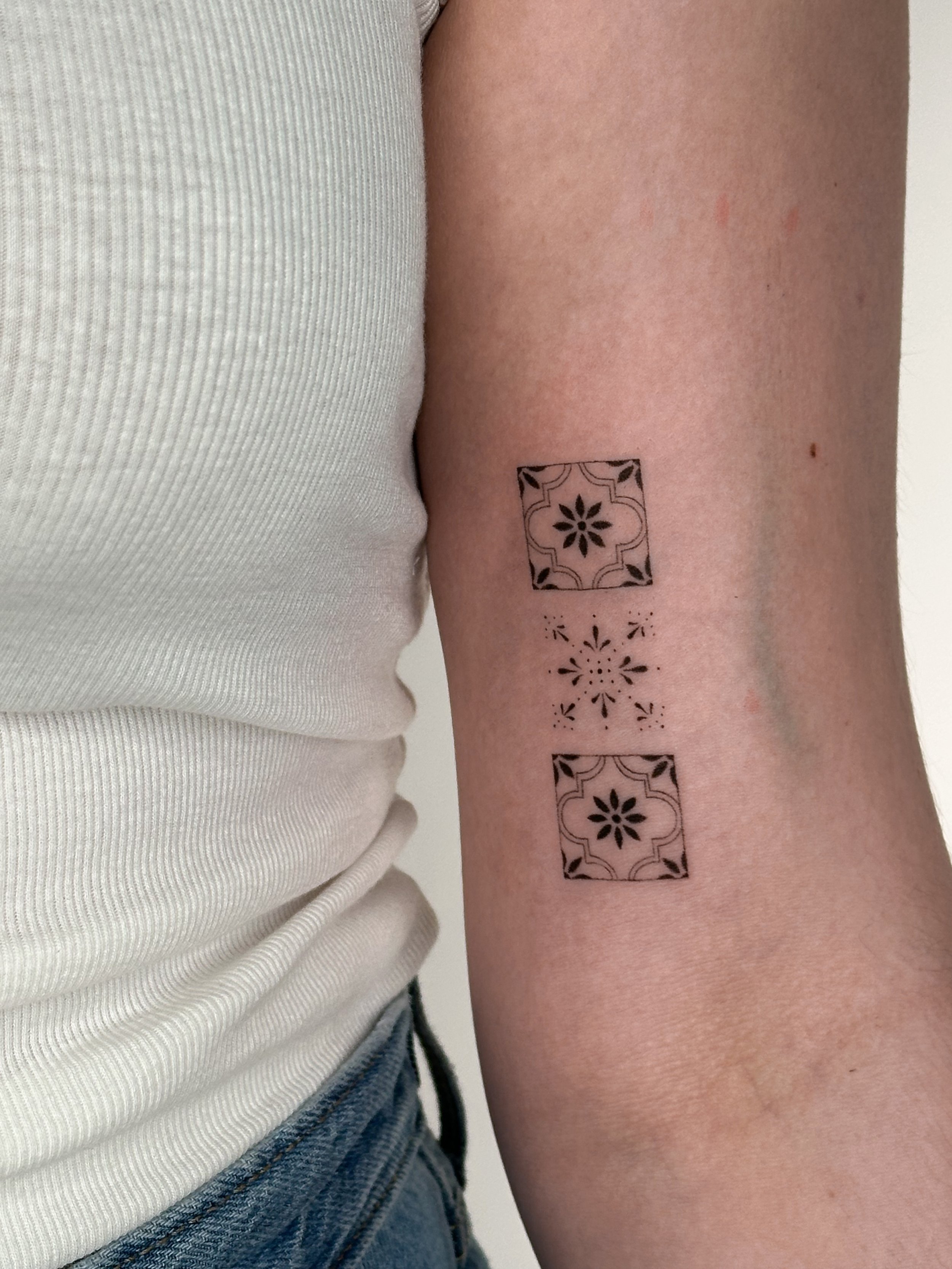 Arm with a tattoo of two black square floral patterns and one smaller geometric design in between.