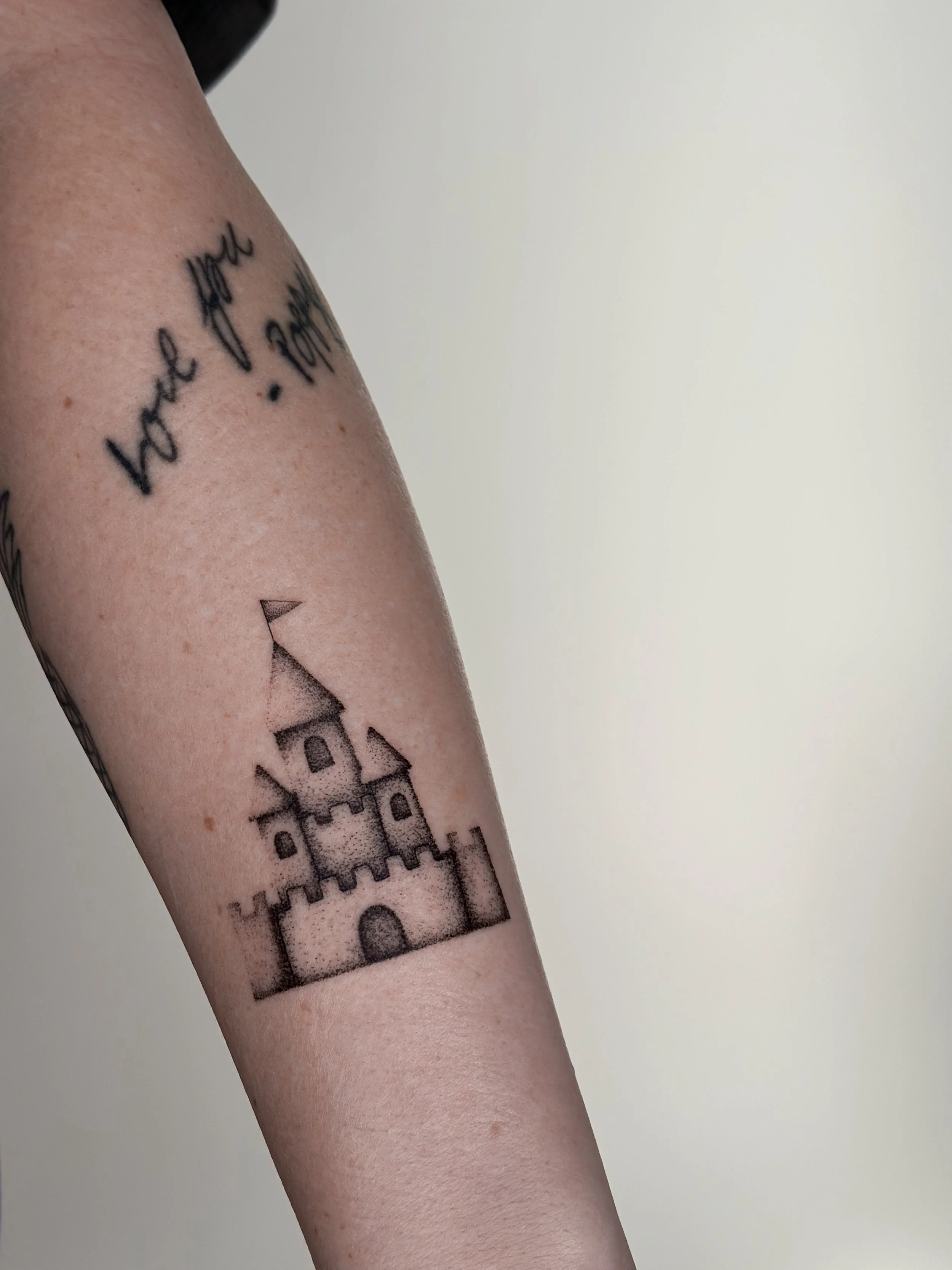 Tattoo of a simple outline of a castle on person's arm.