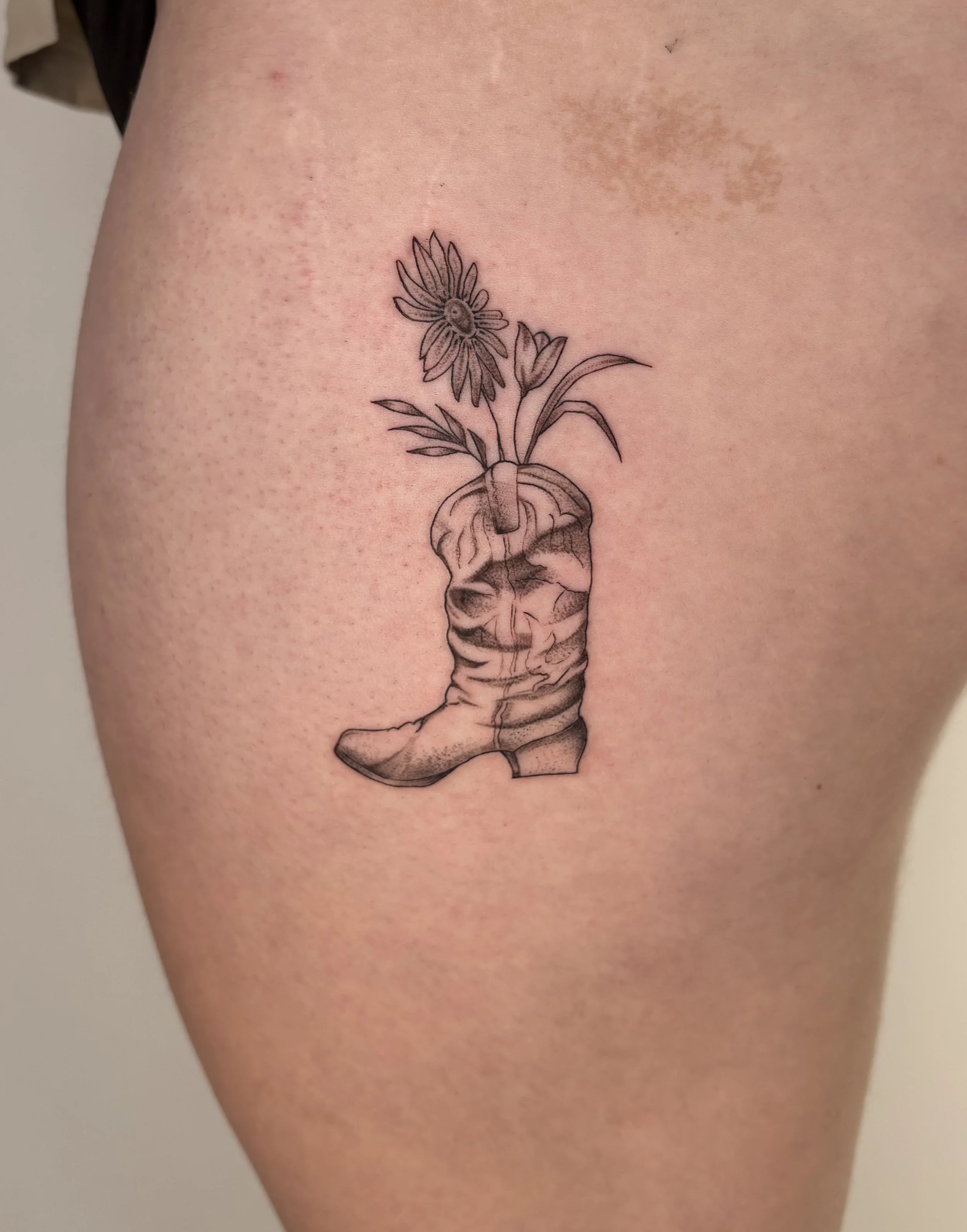 Fineline tattoo of a cowboy boot with flowers growing out of it.