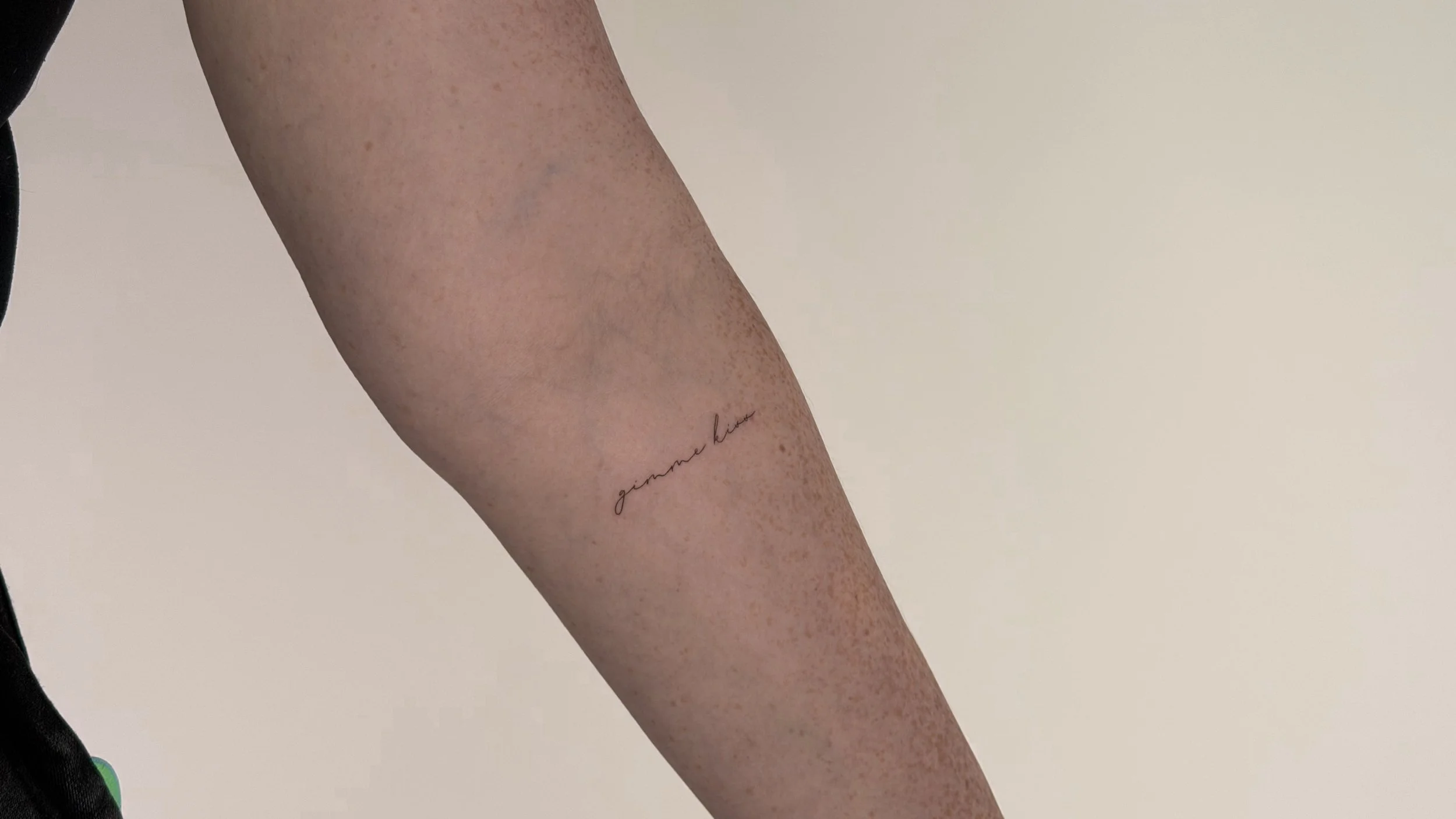 Close-up of a person's forearm with a tattoo that reads 'gimme love' in cursive script.