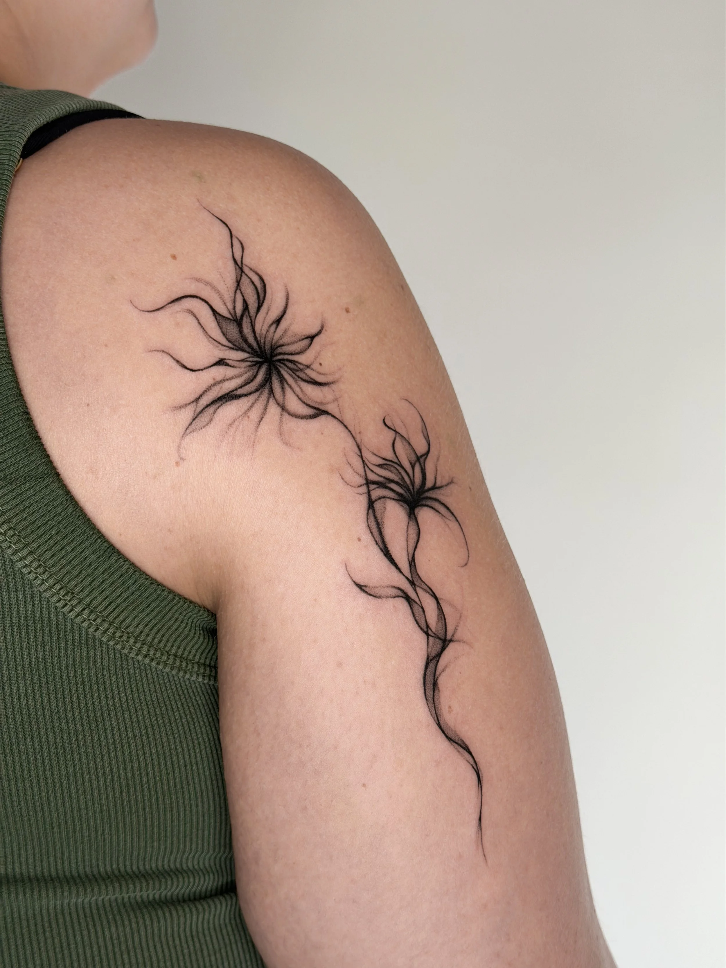 Tattoo of two black floral designs with flowing, wavy lines on a person's upper arm.