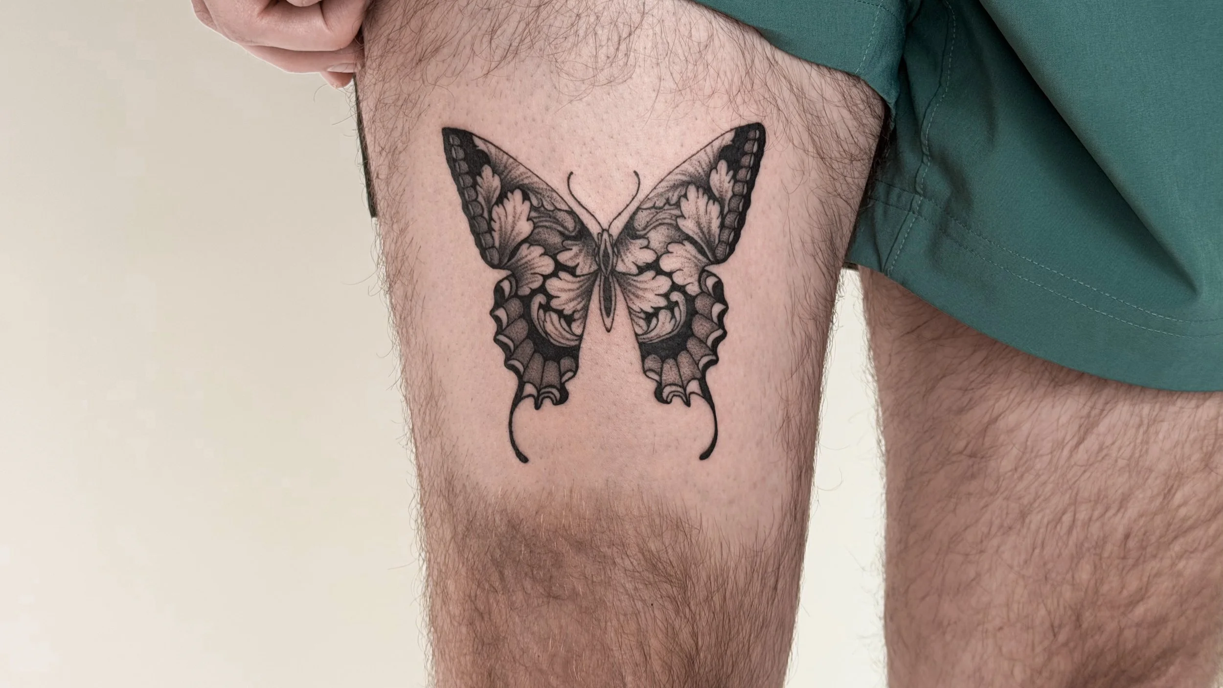 A black and grey butterfly tattoo on a person's upper thigh.