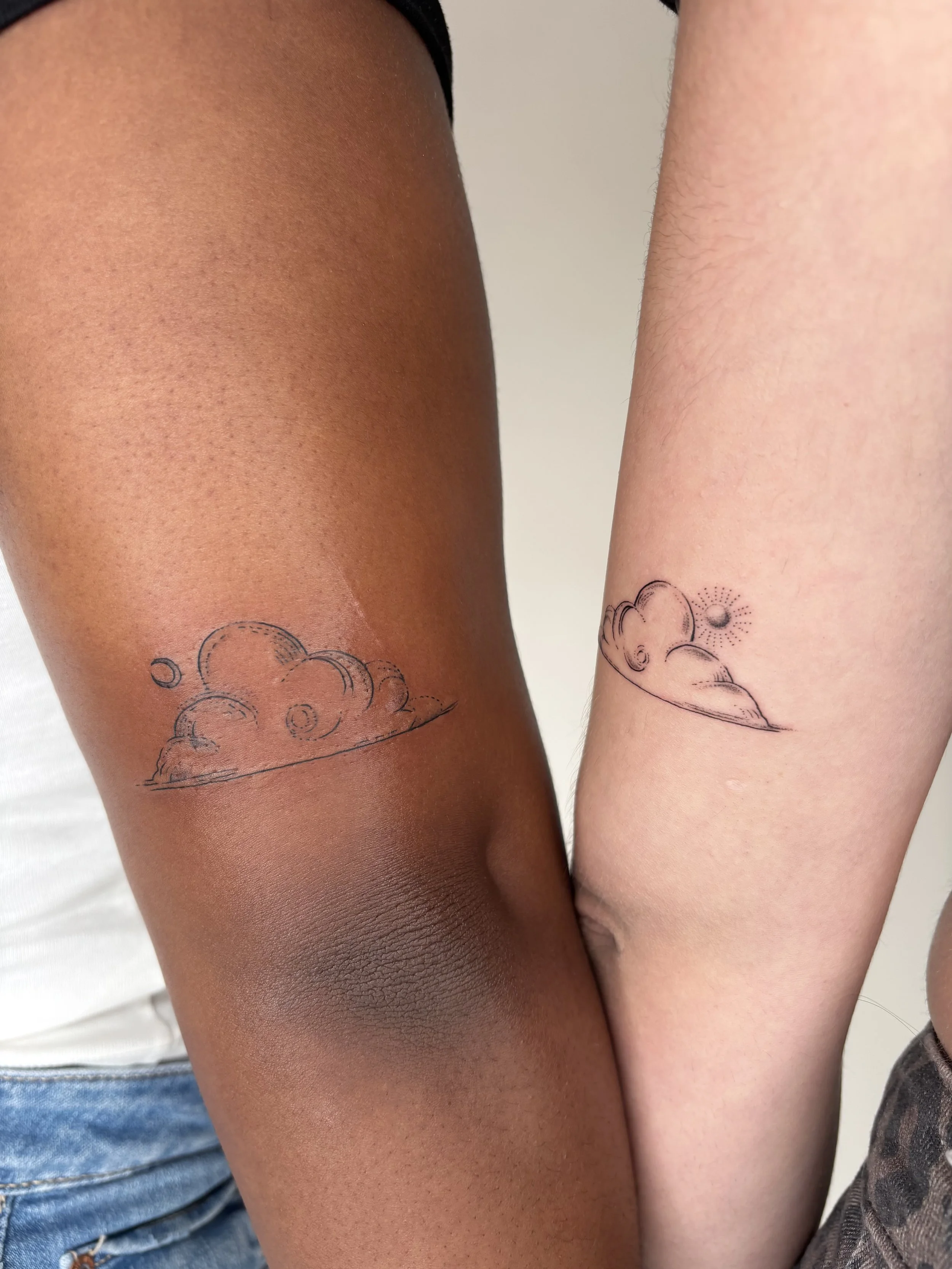 Two people with matching tattoos of clouds with a sun and a moon.