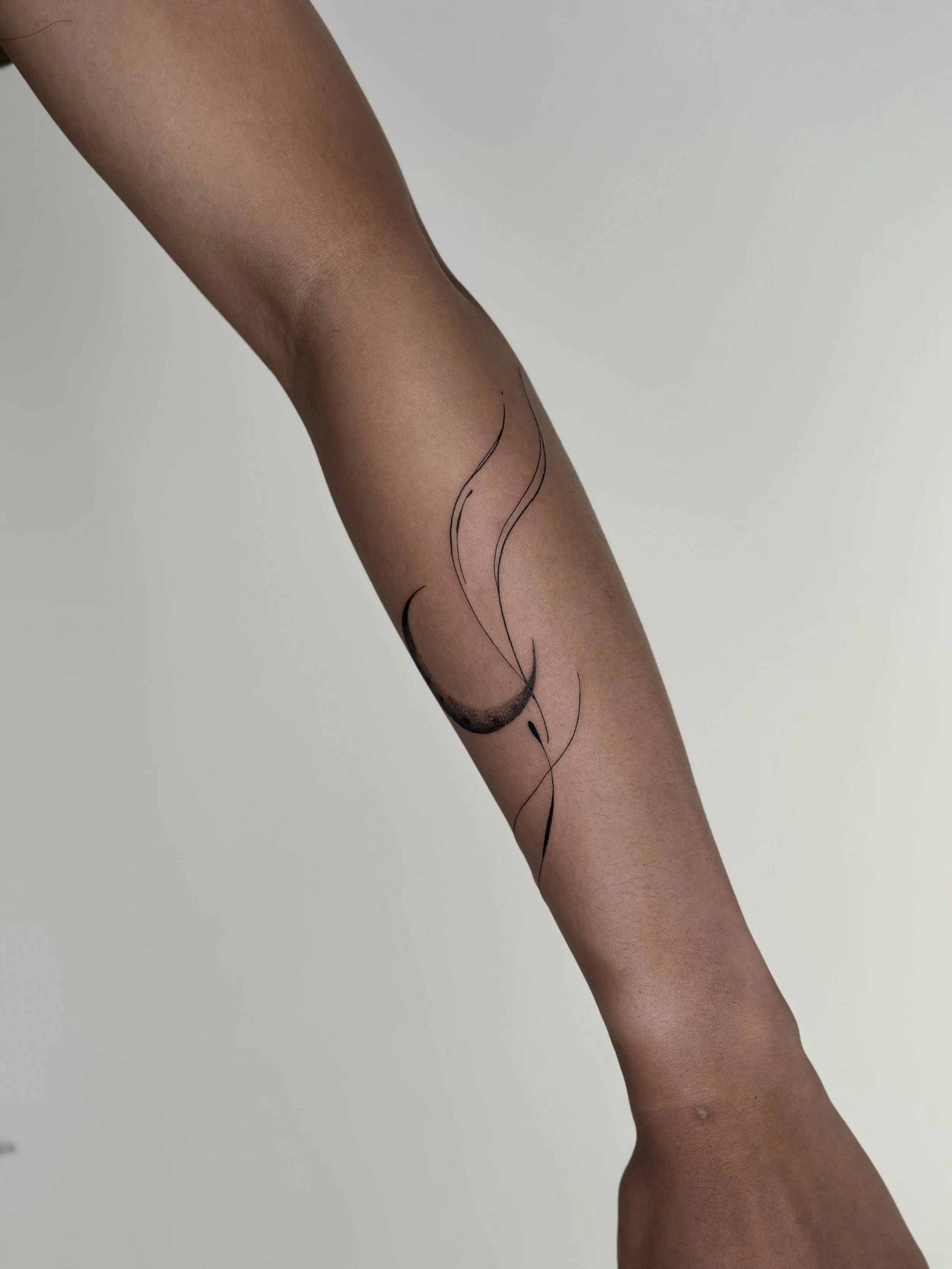 A person's leg with sheer black stocking featuring a minimalist black ink line art design of a moon and flowing lines.