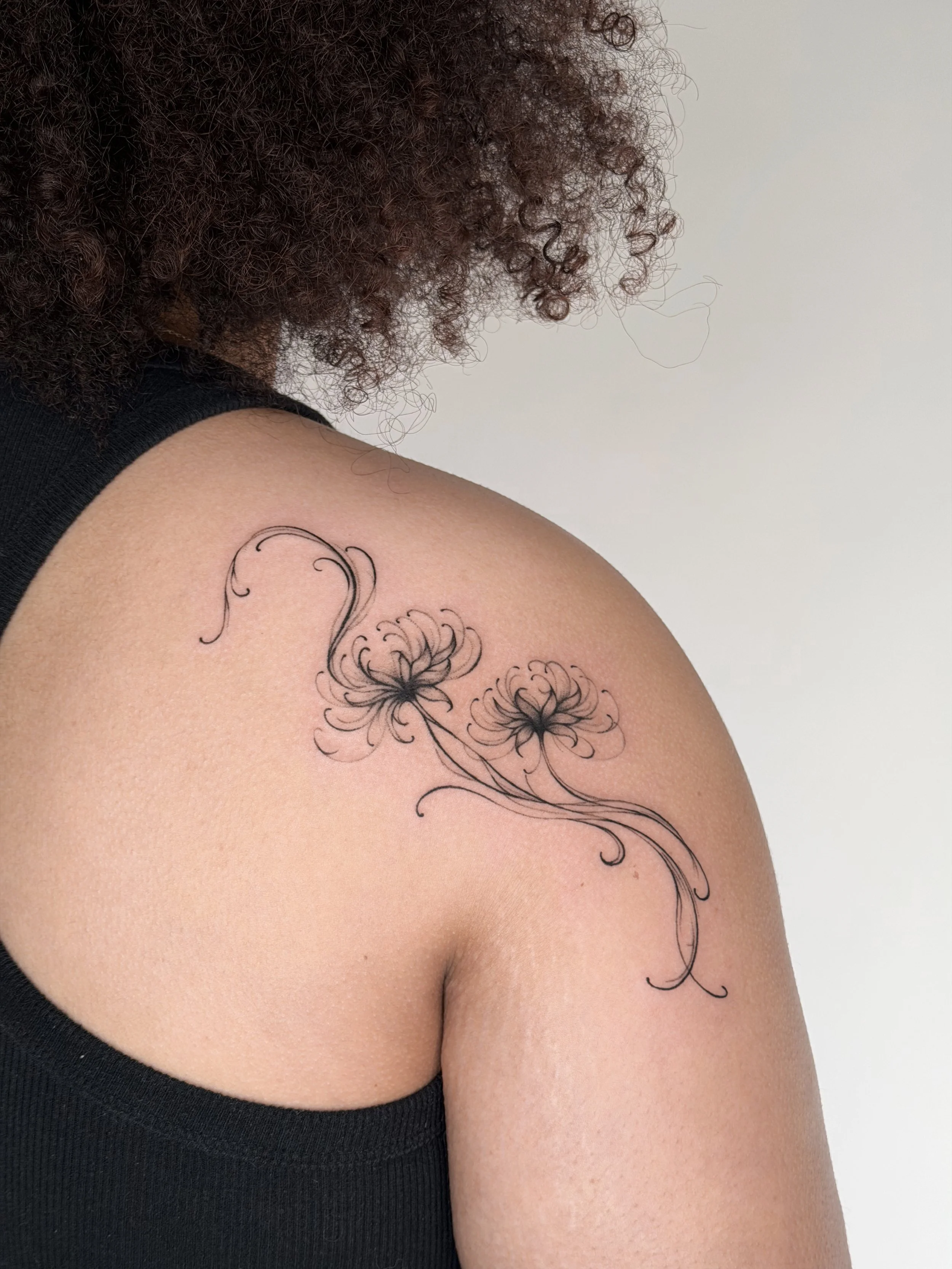 A tattoo of two delicate, swirling flowers on the person's shoulder with long, flowing stems.