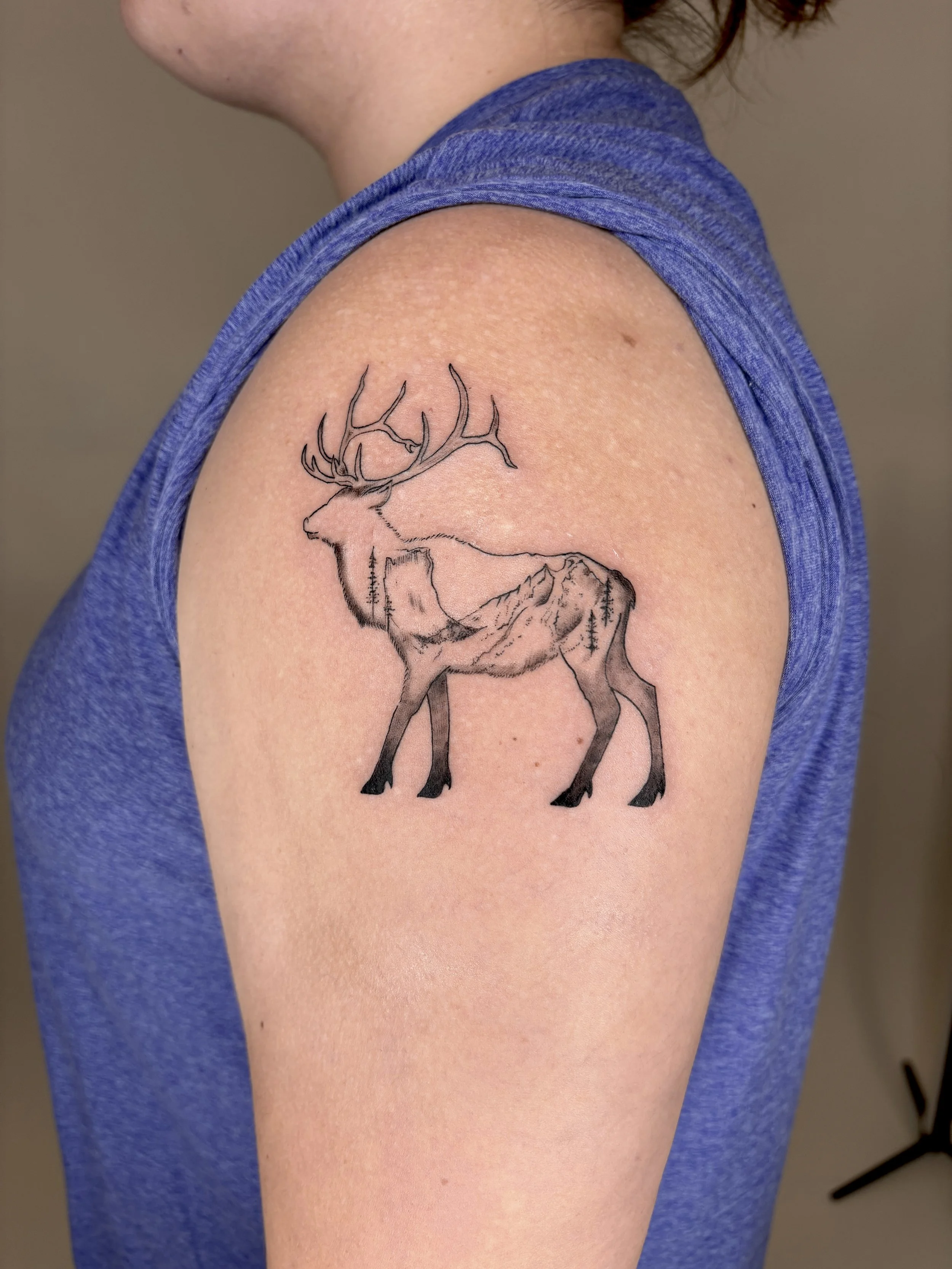 Tattoo on the shoulder of a elk outline with a mountain range scene inside of the outline.