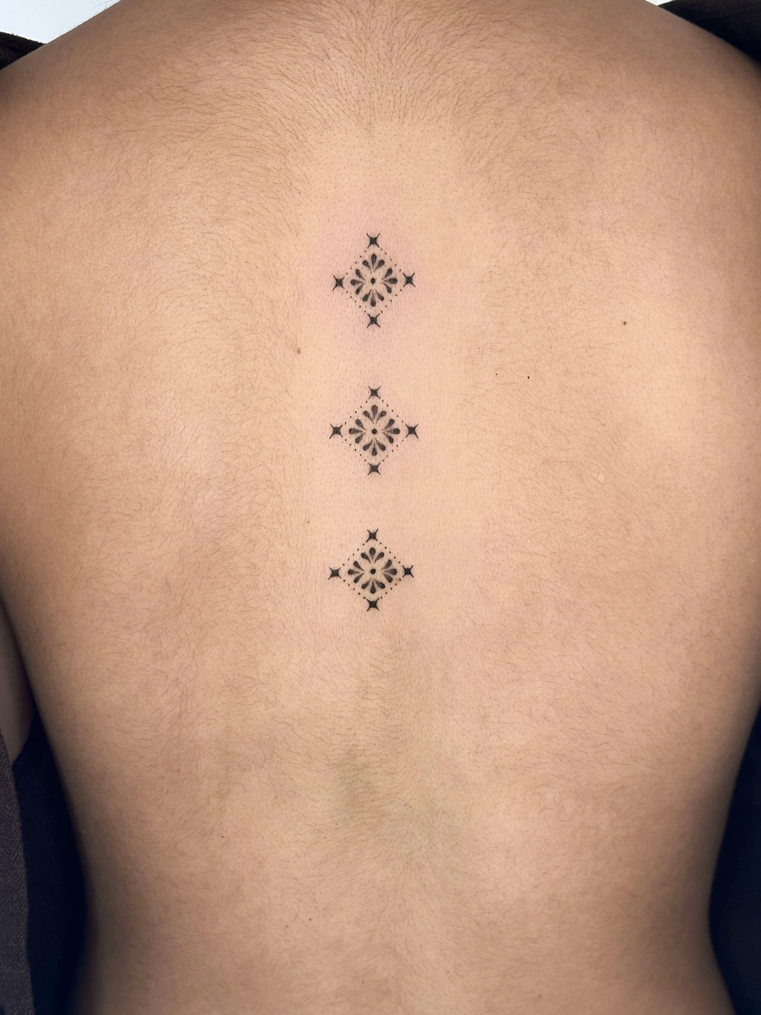 Tattoo of three symmetrical black geometric designs arranged vertically on a person's upper back.
