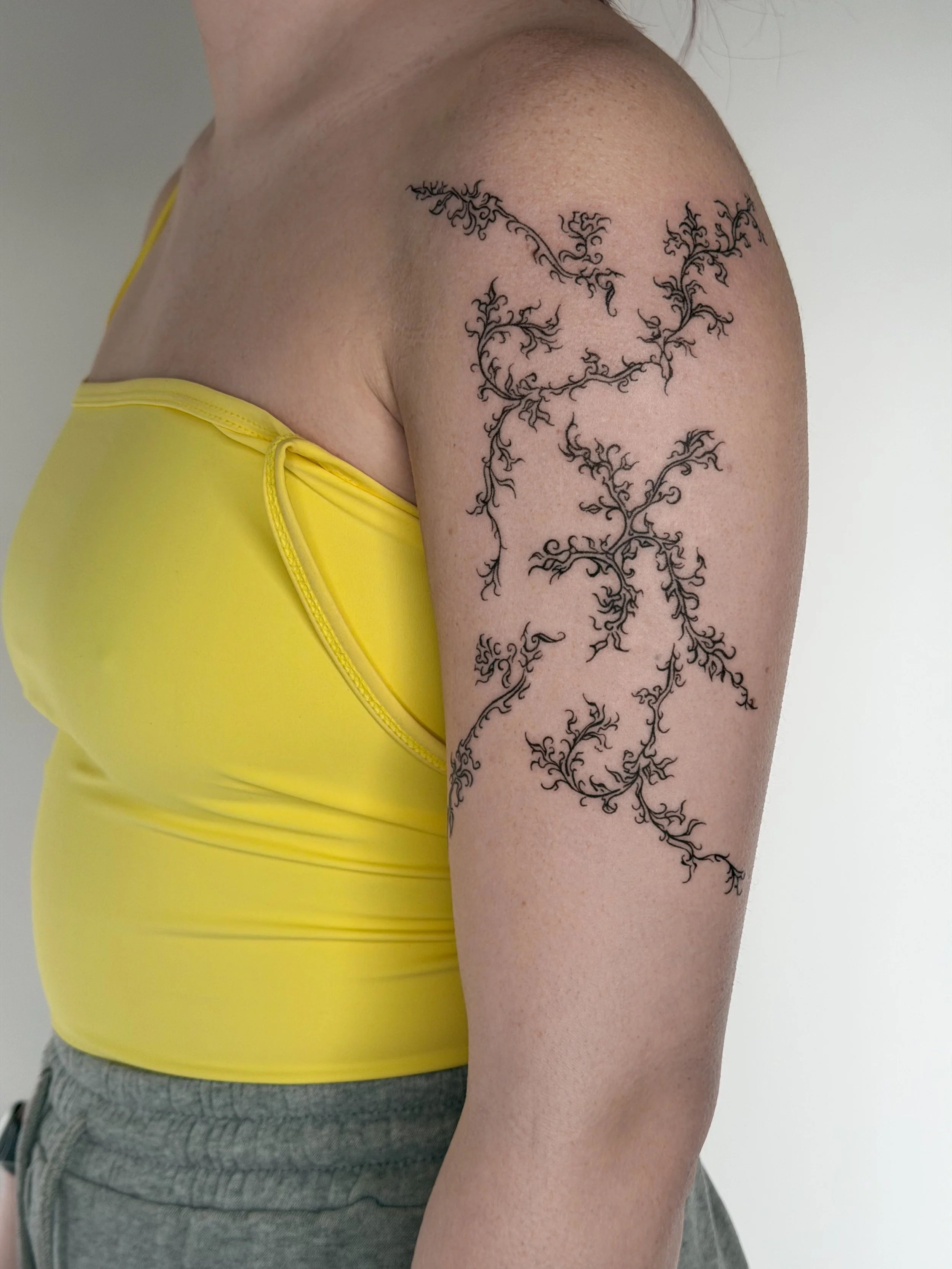 A tattoo of black, intricate, branching tree-like lines on a person's upper arm and shoulder.
