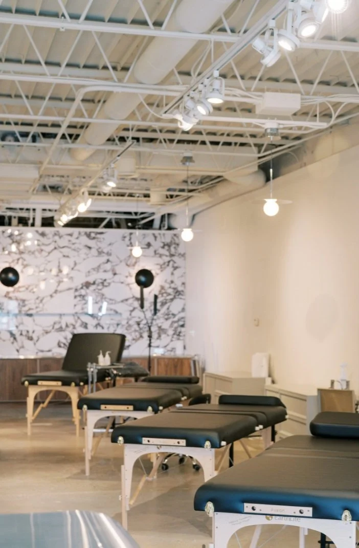 Interior of a modern tattoo studio with adjustable black chairs, marble-patterned wall, and overhead lighting fixtures.