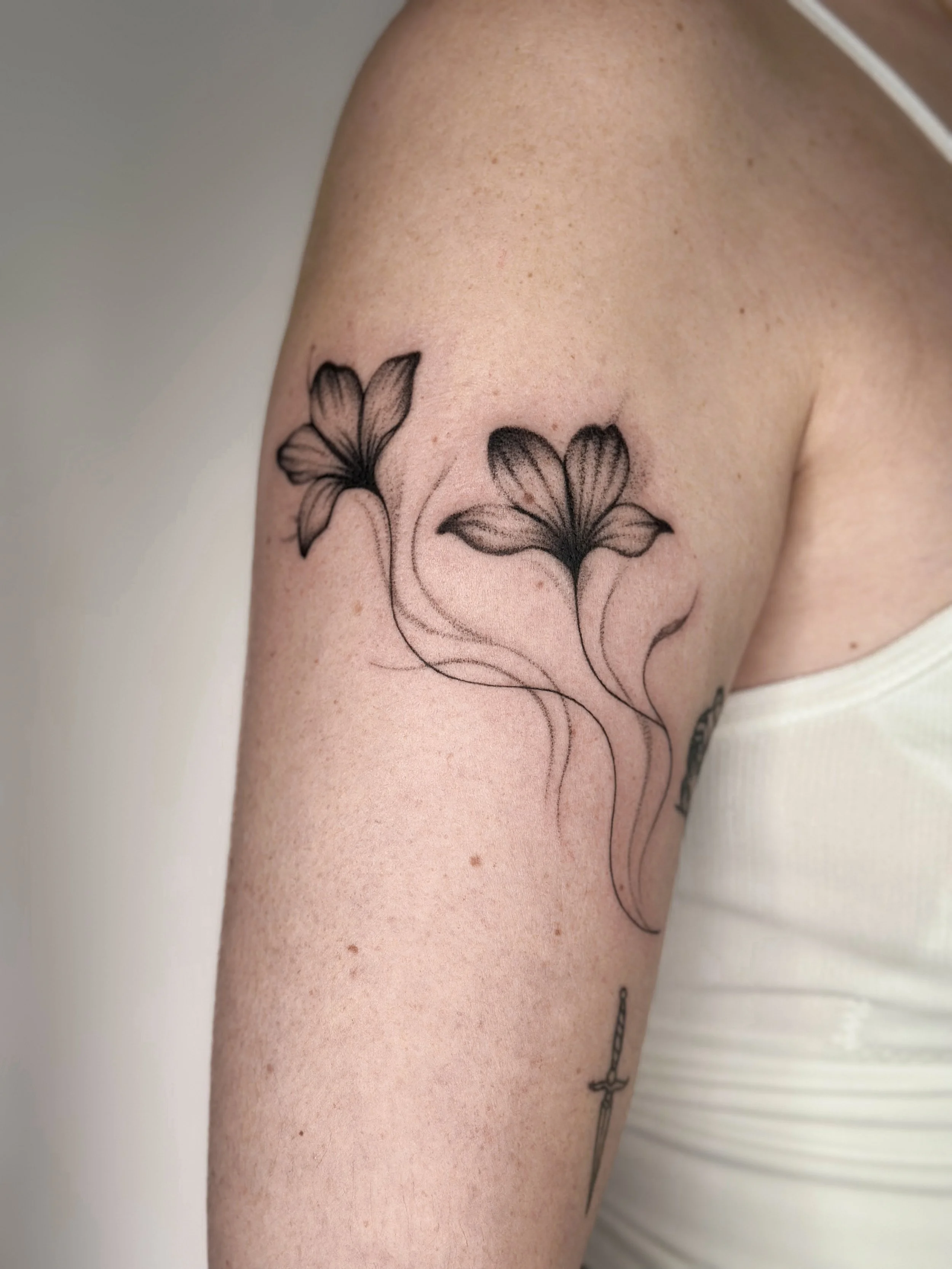 Tattoo of two flowers with flowing stems on upper arm.