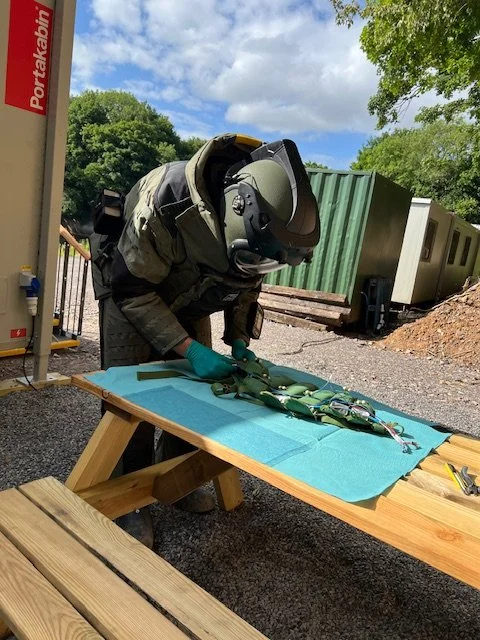 A person in protective gear, including a helmet and gloves, handling multiple items on a table outdoors near train cars.