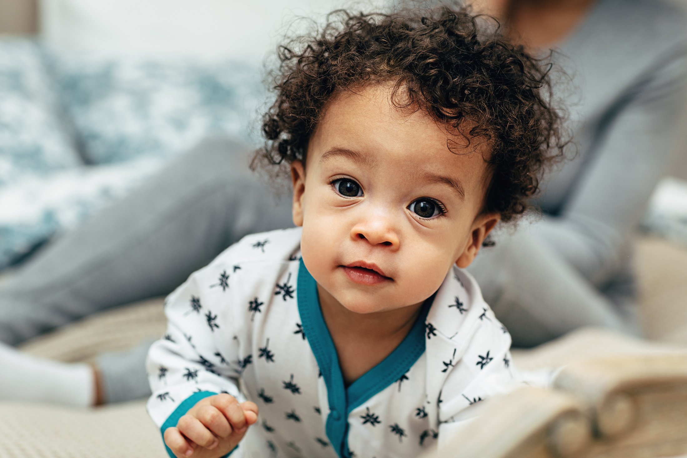 Close-up portrait of a curly-haired baby boy crawling on a bed.