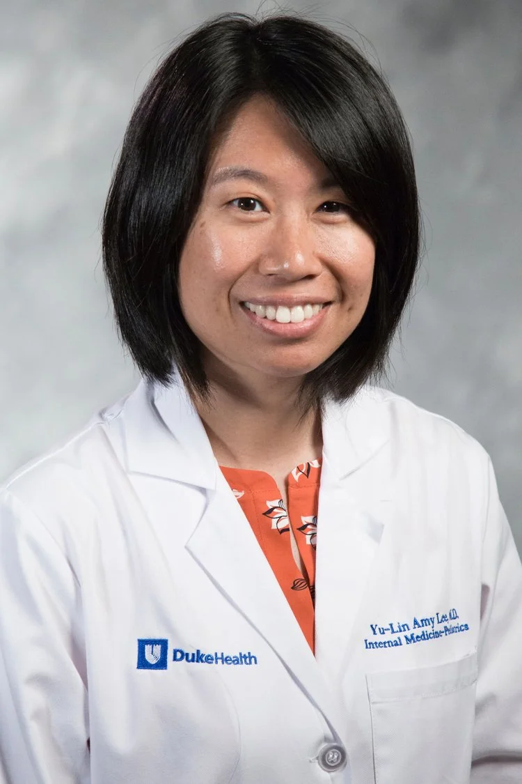 Portrait of a woman wearing a white medical coat with Duke Health logo, smiling at the camera