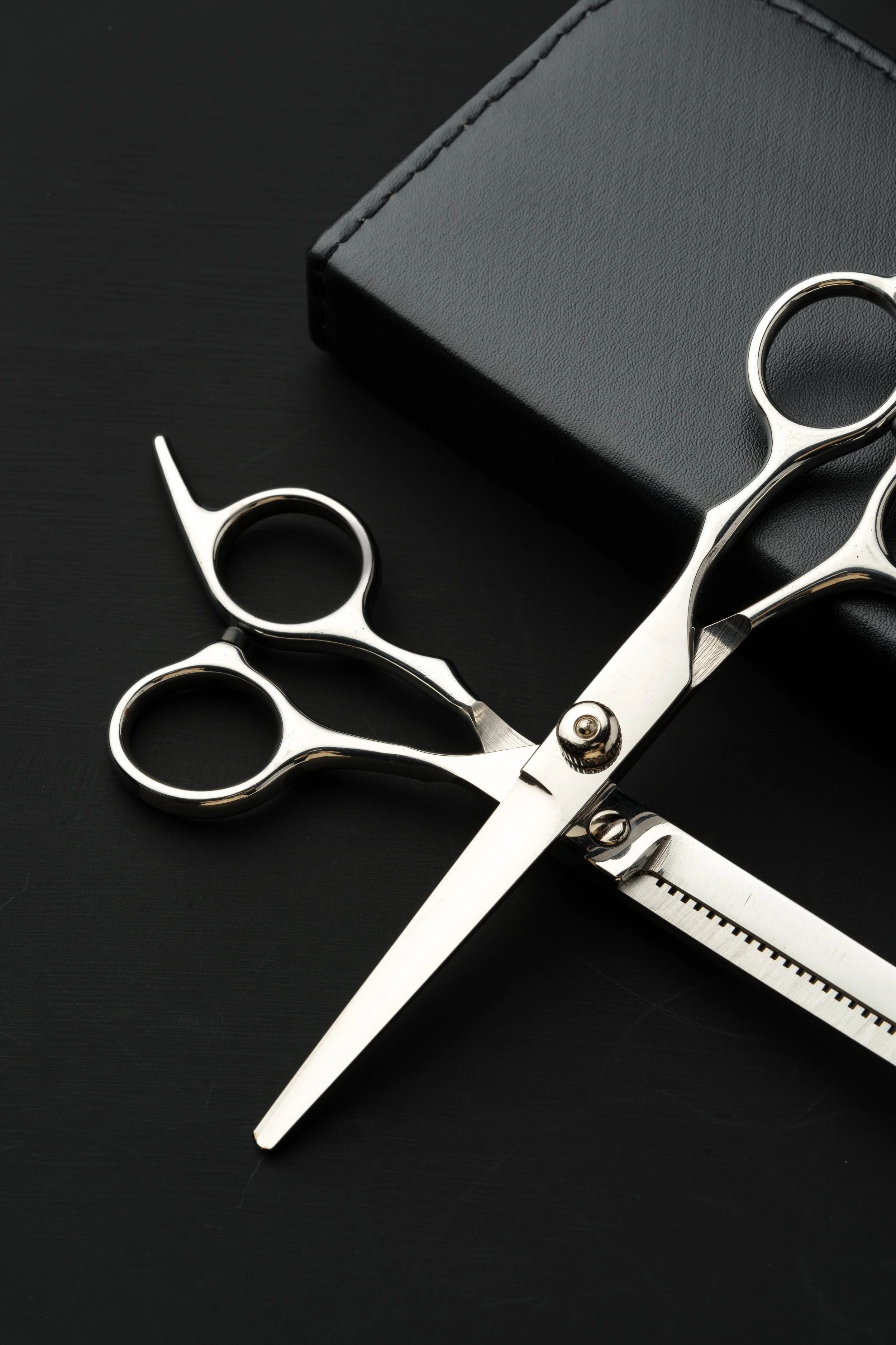 Close-up of hairdressing scissors, a black box, and a black textured surface.