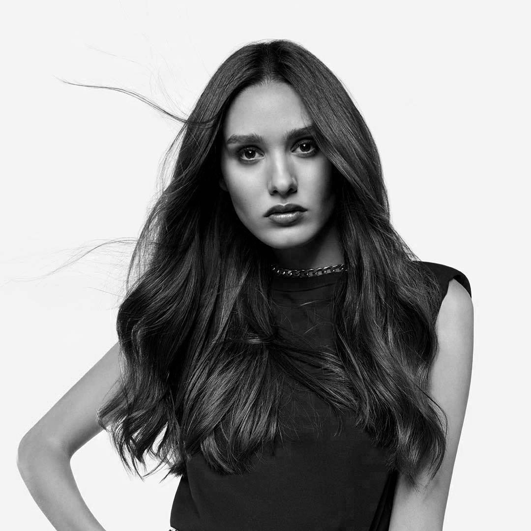 Black and white portrait of a woman with long hair, wearing a sleeveless top and a chain necklace, looking directly at the camera.