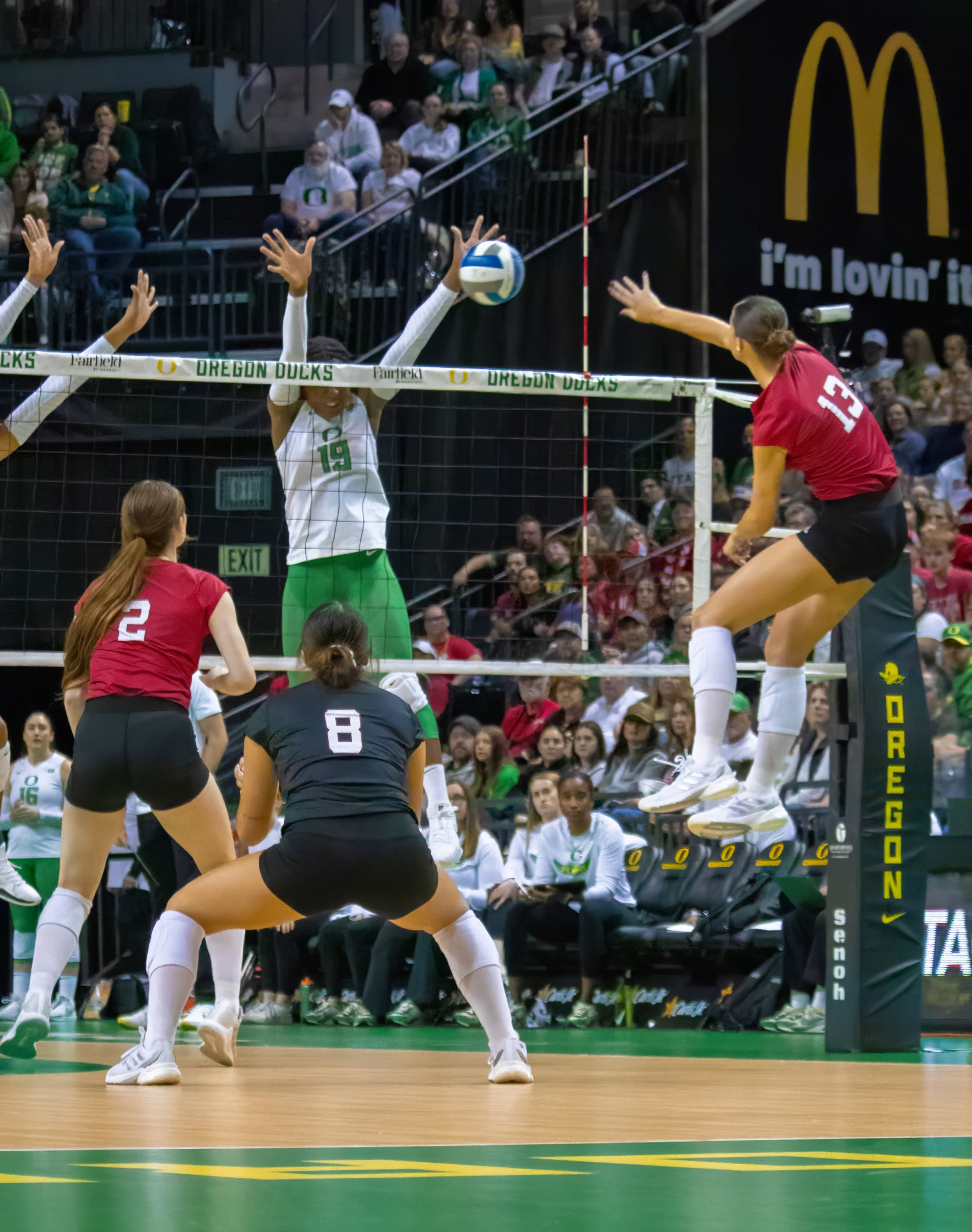 University of Nebraska cornhuskers outside hitter Merritt Beason, #13, leaps off the floor to spike ball over court as University of Oregon duck outside hitter Michelle Ohwobete, #19, attempts to block. Photo by Emily Manciu