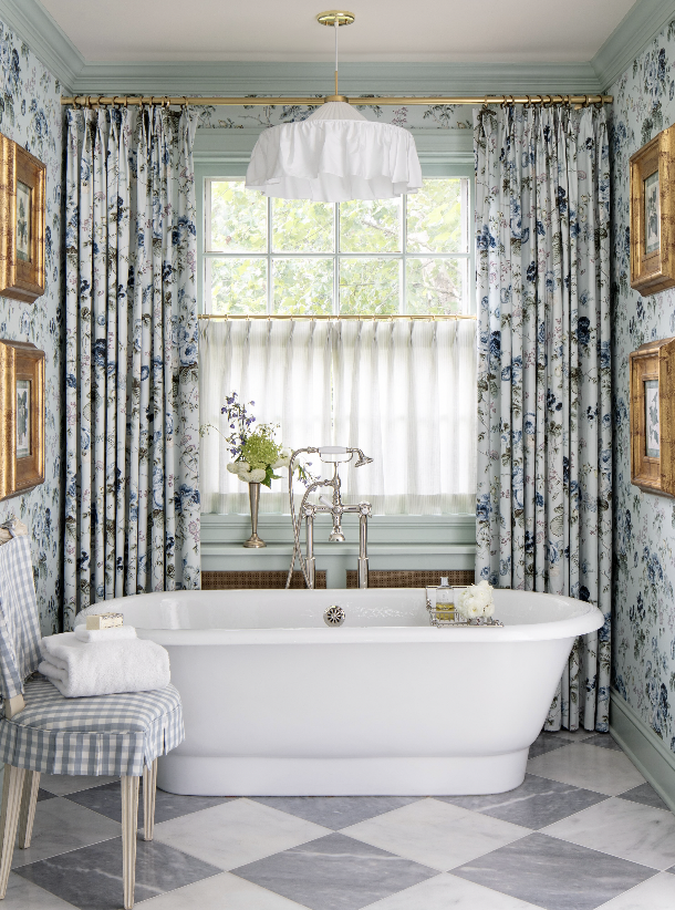 A vintage-style bathroom with a white clawfoot bathtub, floral curtains, and framed artwork on the walls.